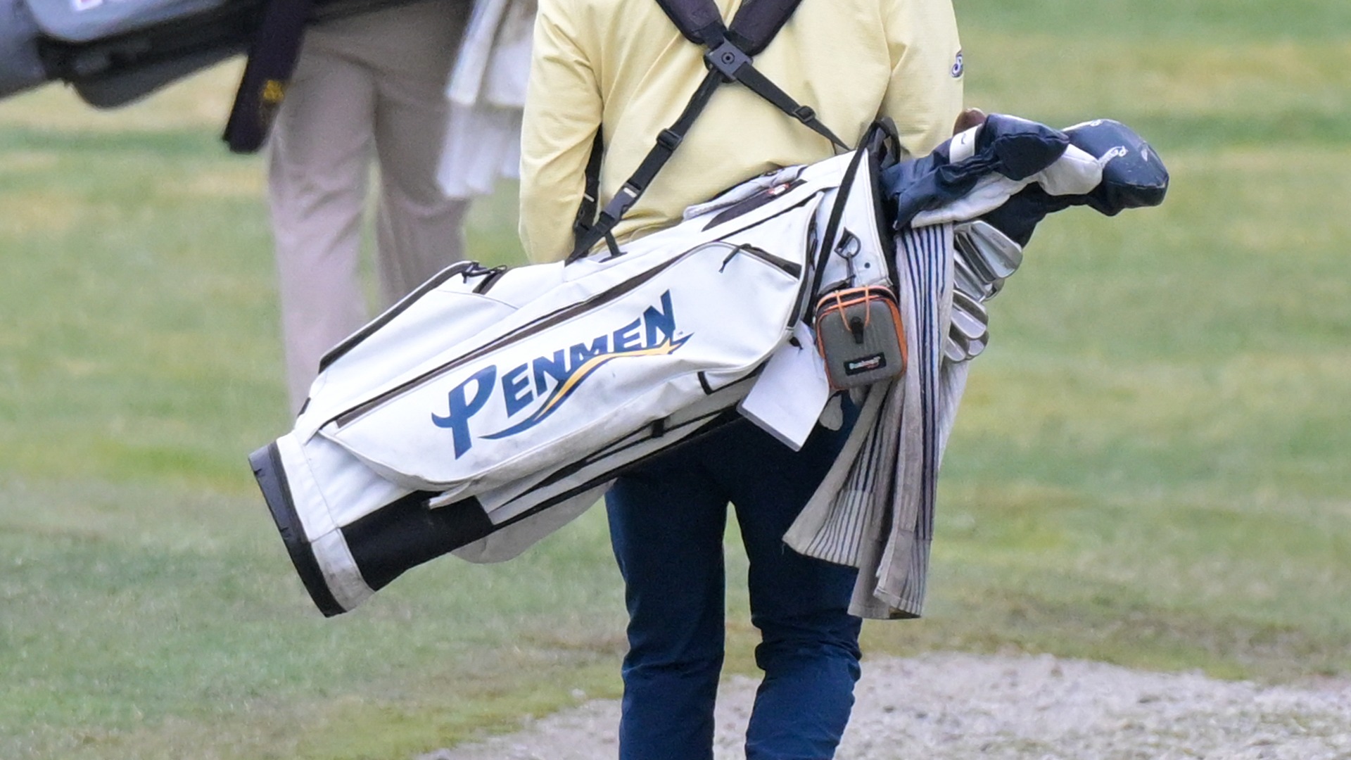 a member of the SNHU men's golf team walking with his Penmen bag on his back