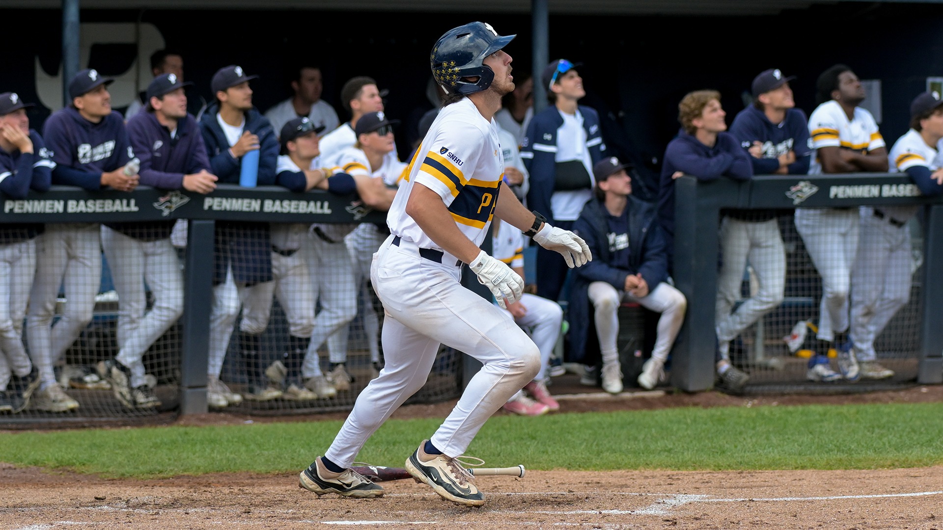 Cumiskey watching his hit, while his teammates also watch from the dugout in the background