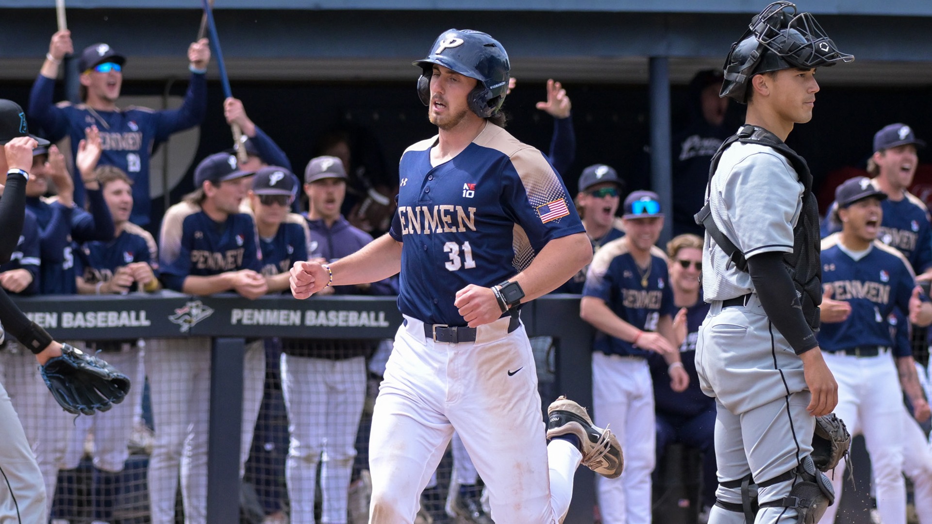 Casey Cumiskey crossing home plate with the opposing catcher in the foreground and his teammates celebrating in the dugout in the background