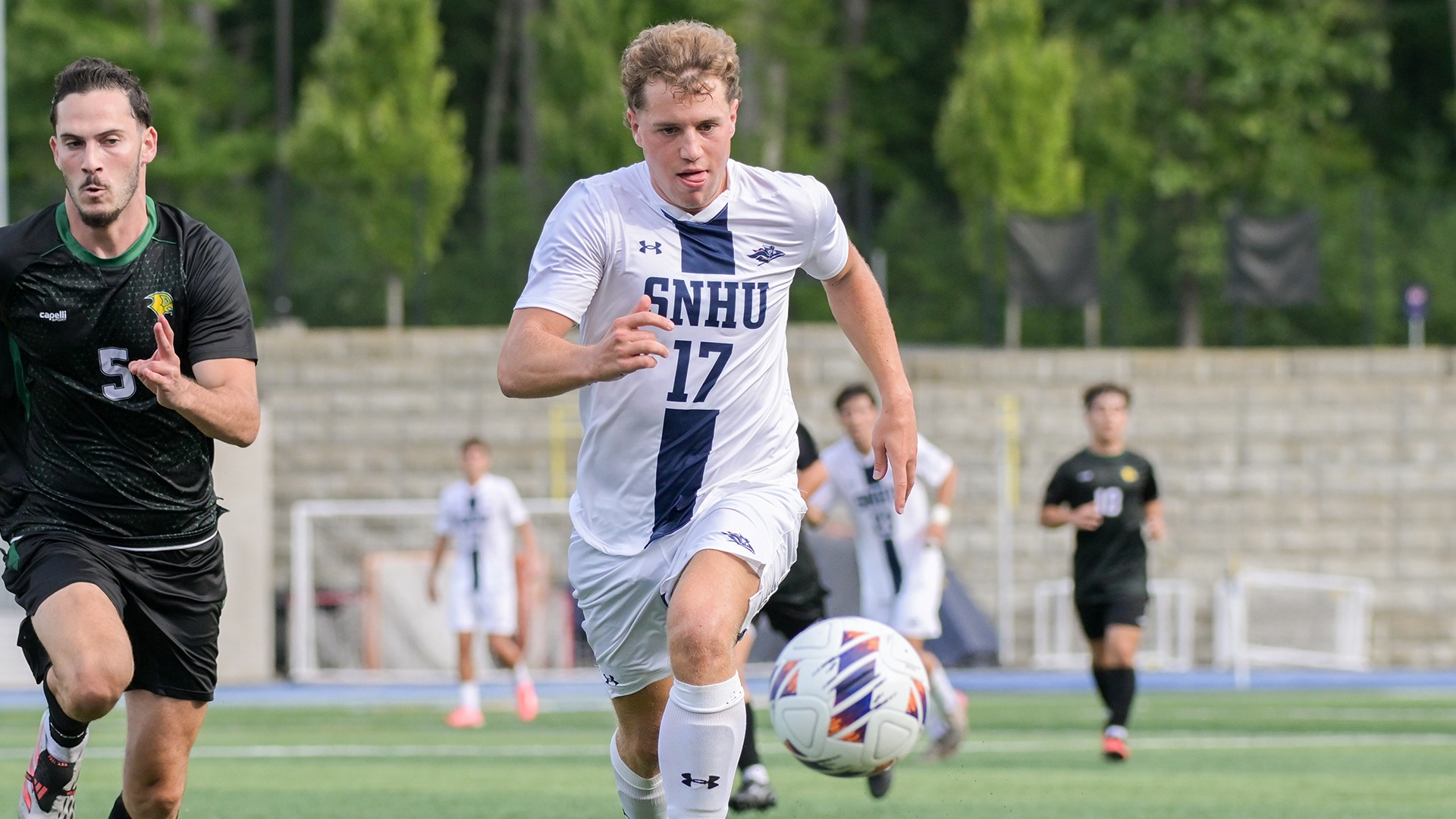 Charlie Preus running after the ball in the foreground, with a defender in the background