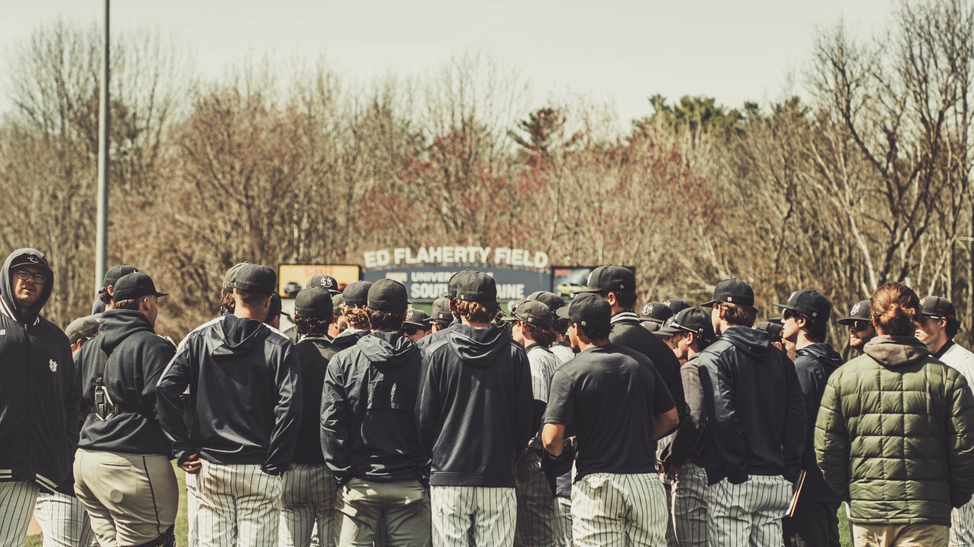 Huskies' Baseball huddling near Ed Flaherty Field Scoreboard