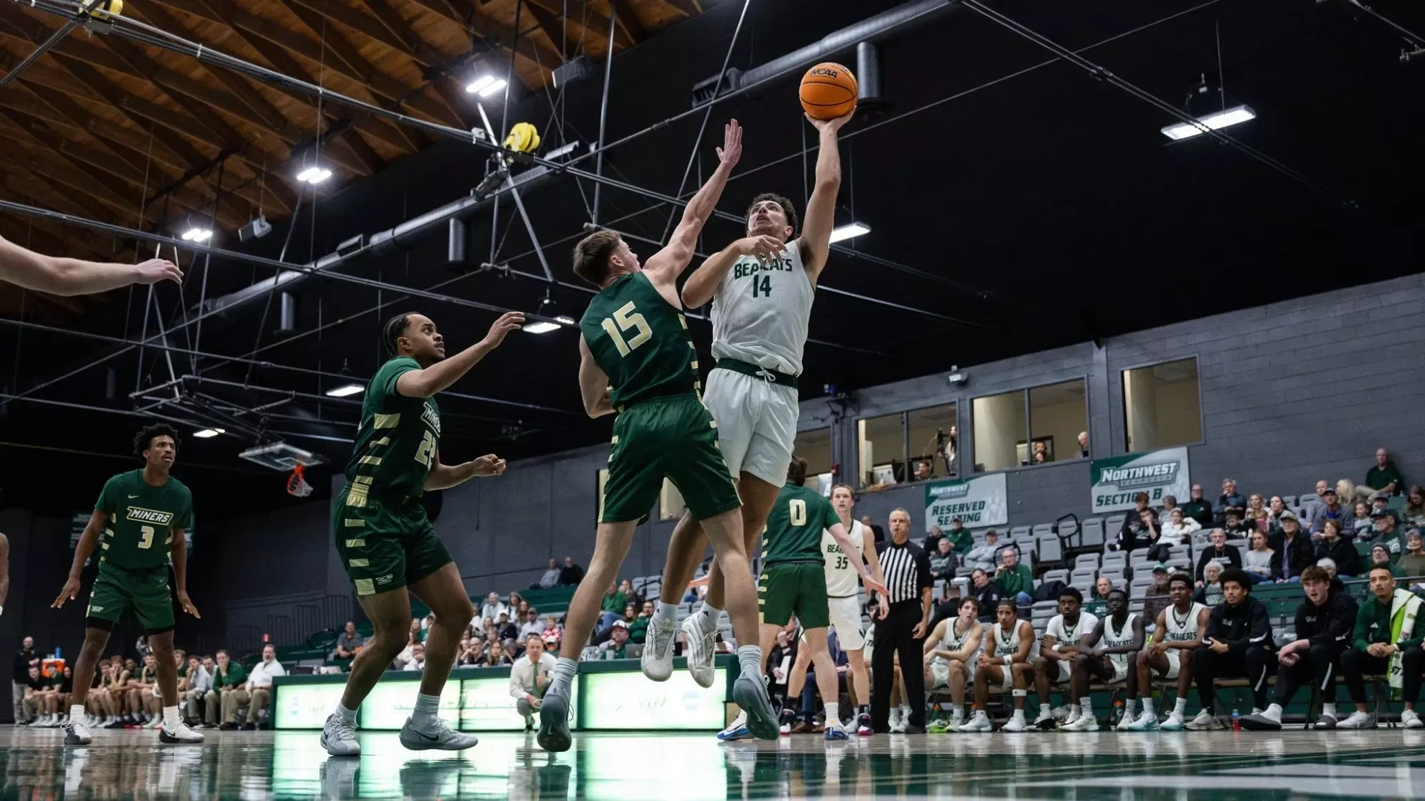 Basketball Photo of Garrett Hines jumping up to block a shot being taken by a NWMSU player
