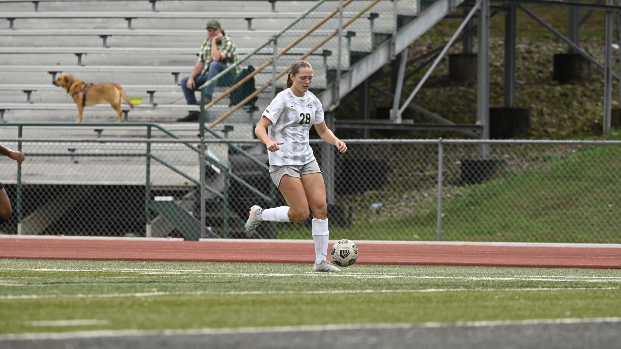 Adriana Benassi dribbling the soccer ball down the field with a man and dog in the background