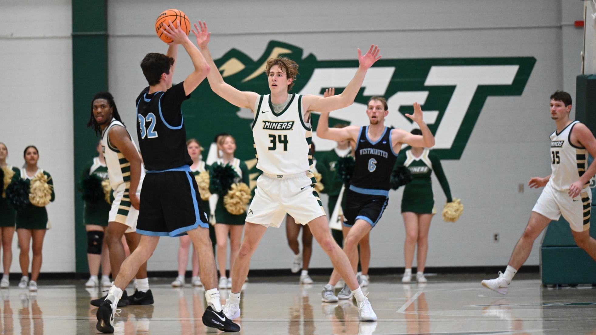 Photo of men's basketball player in a defense stance with his arms spread wide as he attempts to prevent a pass by an opposing point guard