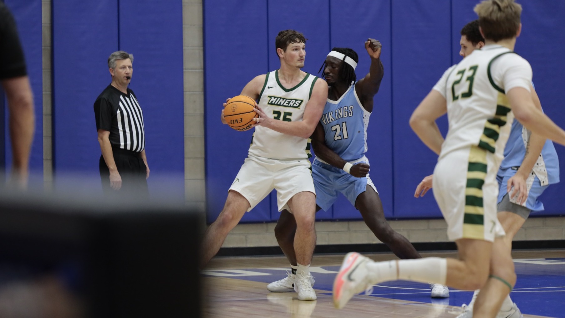 Photo of Missouri S&T men's basketball athlete holding the basketball in the paint and leaning into a defender who has his hands up to prevent a shot or pass