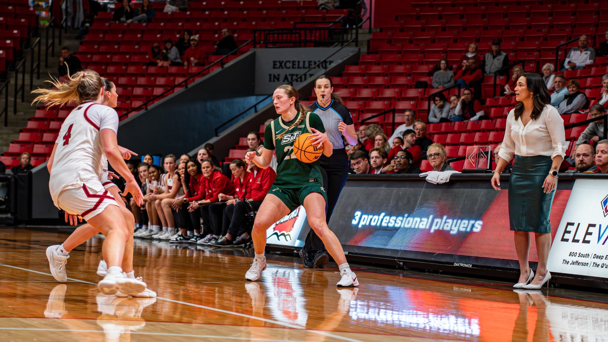 Adriana Benassi dribbling the ball with two Drury defenders next to her and head coach Kira Carter to the right of her.