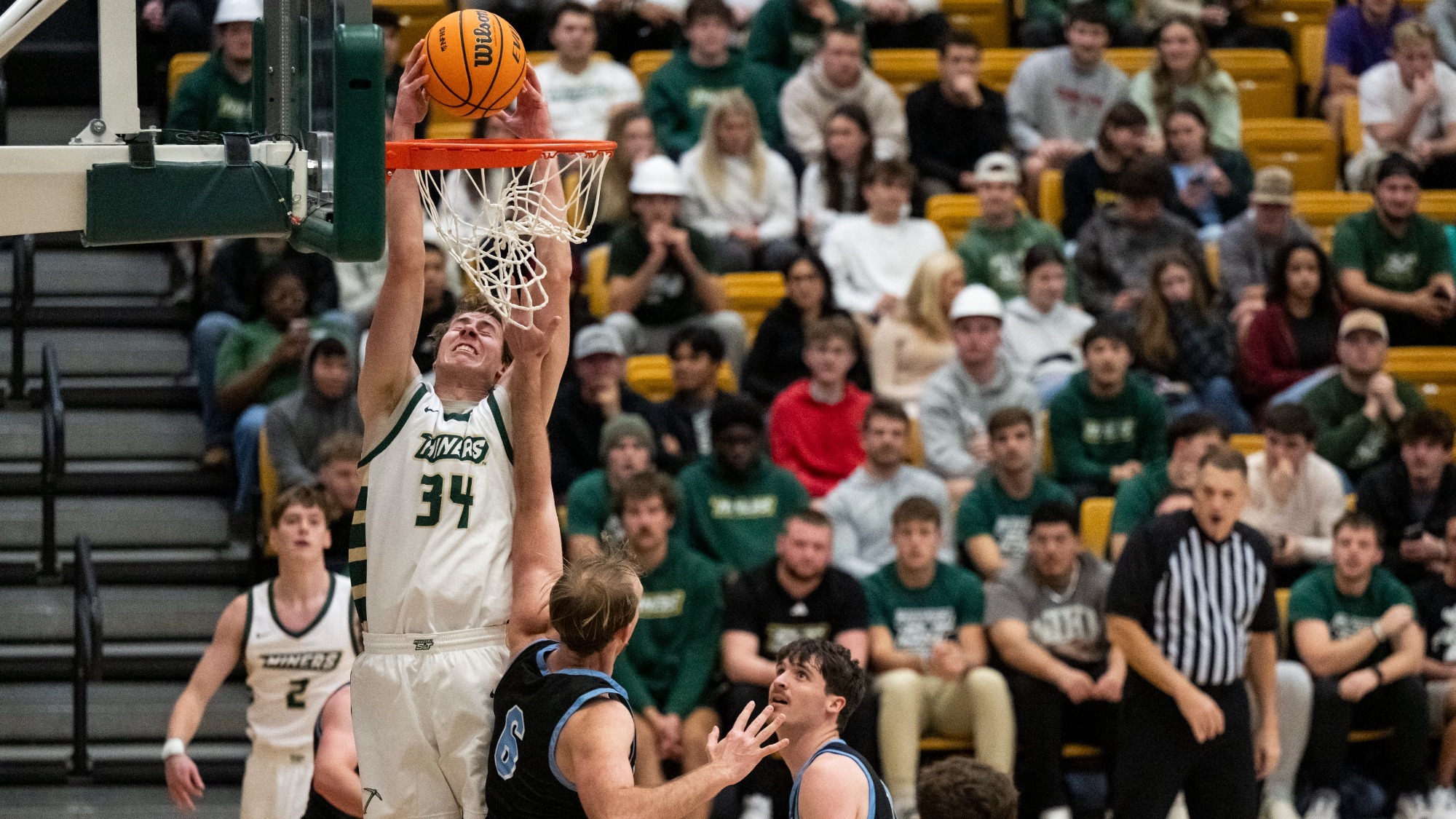Andrew Young of Missouri S&T rises above defenders to dunk the basketball with two hands during a men’s basketball game, as opponents attempt to contest the play and a packed crowd watches from the bleachers behind the basket.