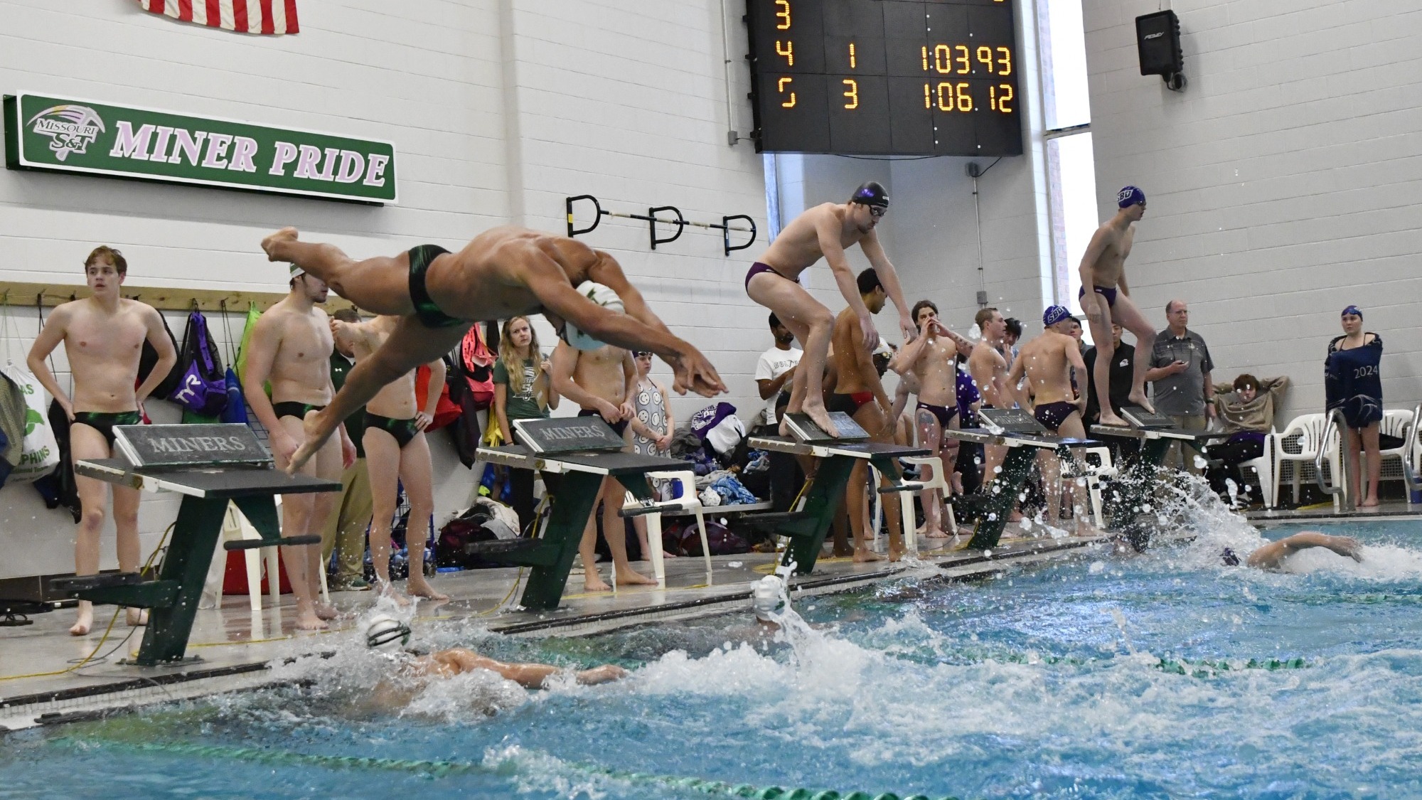 Photo of S&T swimmer diving into the pool at Gale Bullman during a swim meet during a relay race where his teammate has just touched the wall... opposing swimmer to his left about to jump in too