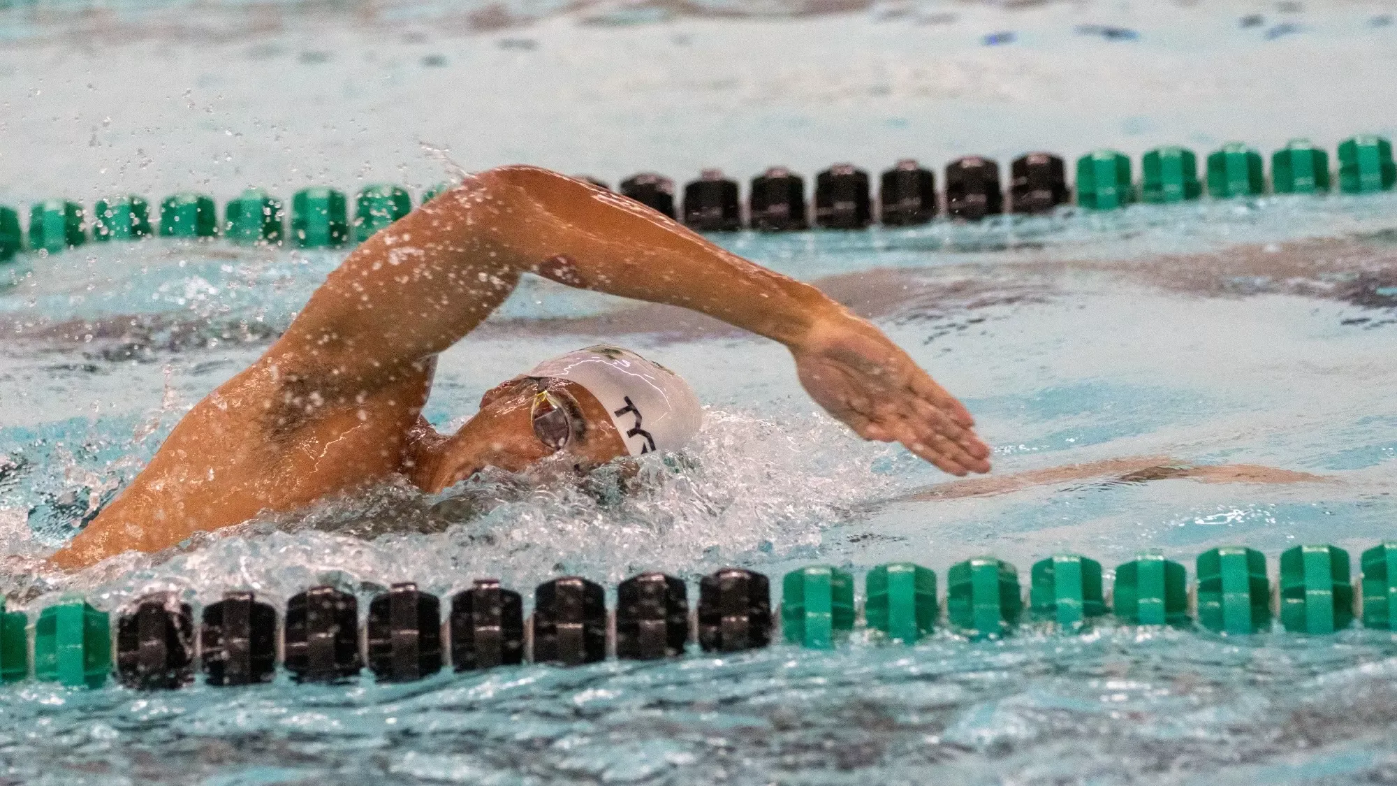 Closeup shot of S&T swimmer wearing a white swim cap while doing the freestyle in the S&T pool during a home meet