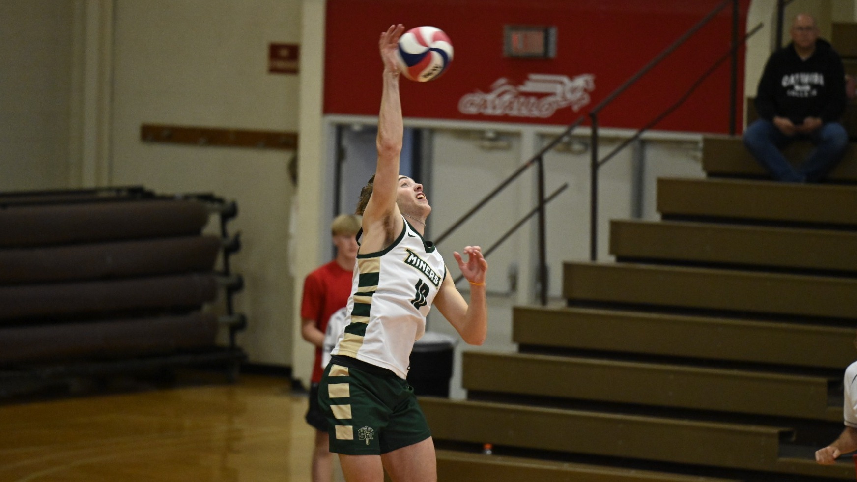 Missouri S&T men's volleyball player nate meyer wearing a white and green jersey while serving the ball in a match at Maryville