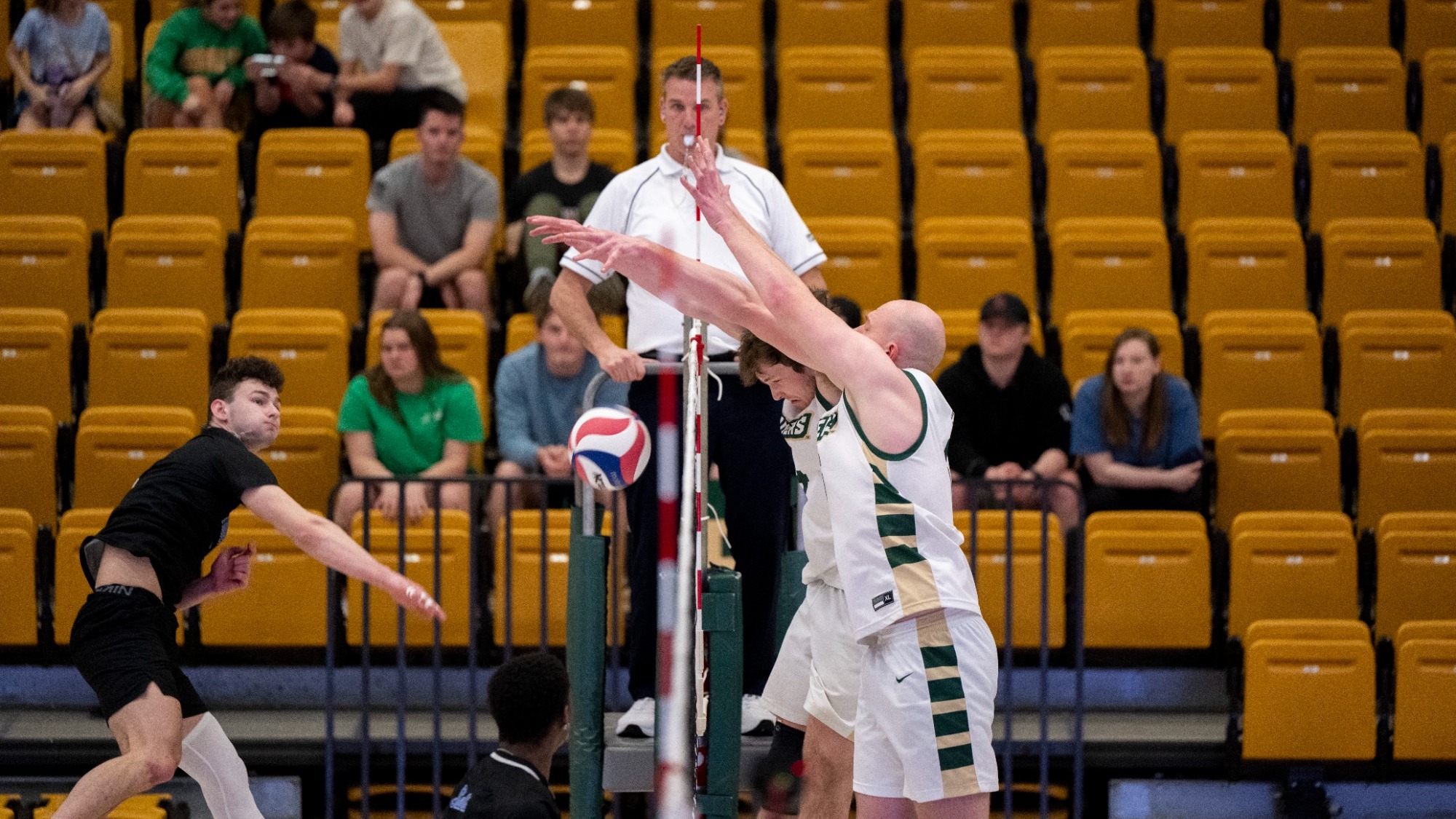 Missouri S&T men's volleyball athletes Aaron Sallade and Caleb Rohlwing wearing white jerseys while jumping at the net and blocking an opponents' attack attempt