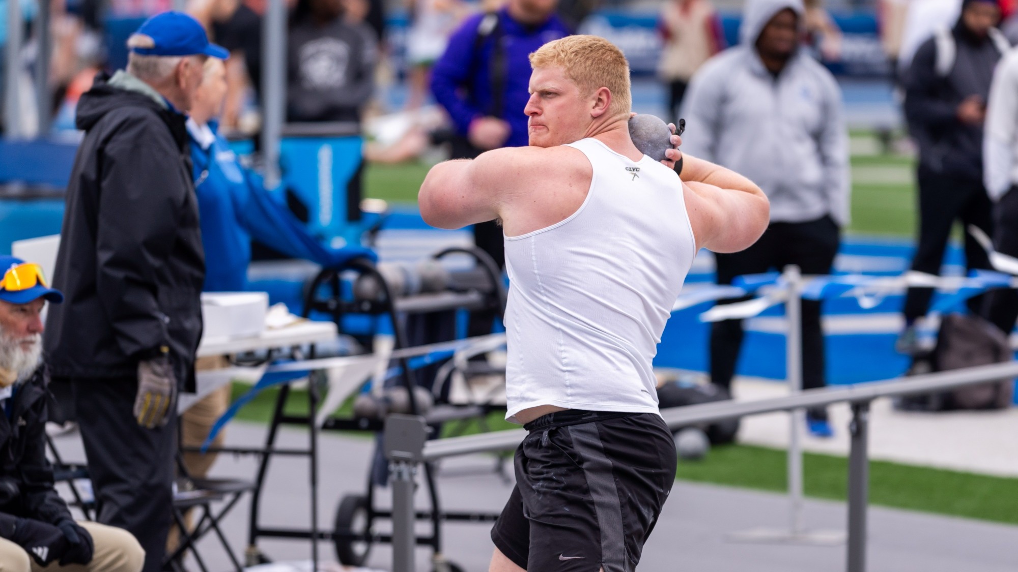 Missouri S&T field athlete Owen Fraser wearing a white uniform and holding a shot up to his chin as he gets ready to throw for the shot put at the Drake Relays
