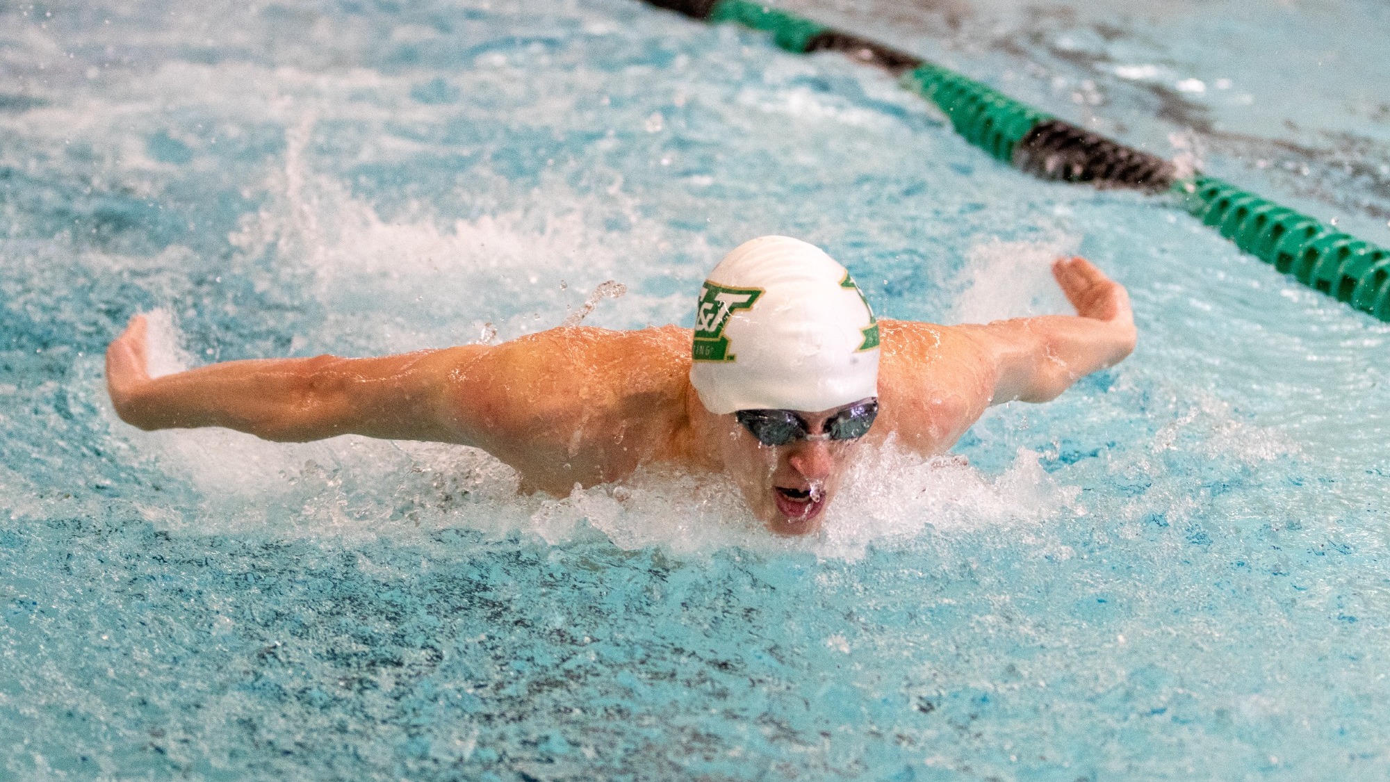 Missouri S&T swimmer wearing white cap while doing the butterfly stroke during a swim meet at Gale Bullman