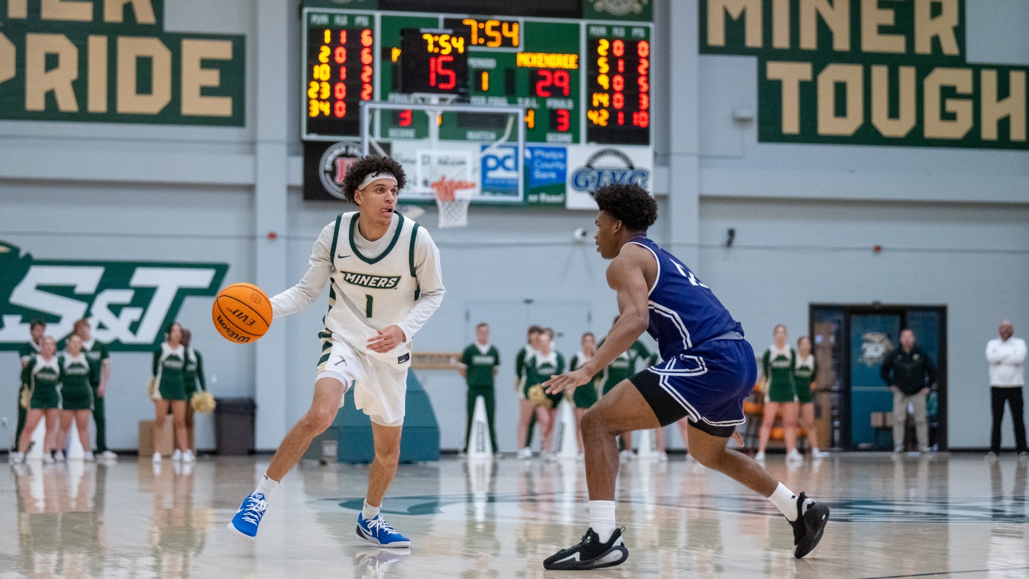 Missouri S&T men's basketball player Blaise Beauchamp wearing a white jersey and dribbling the basketball above the three point line while a McKendree defender blocks his path to the basket