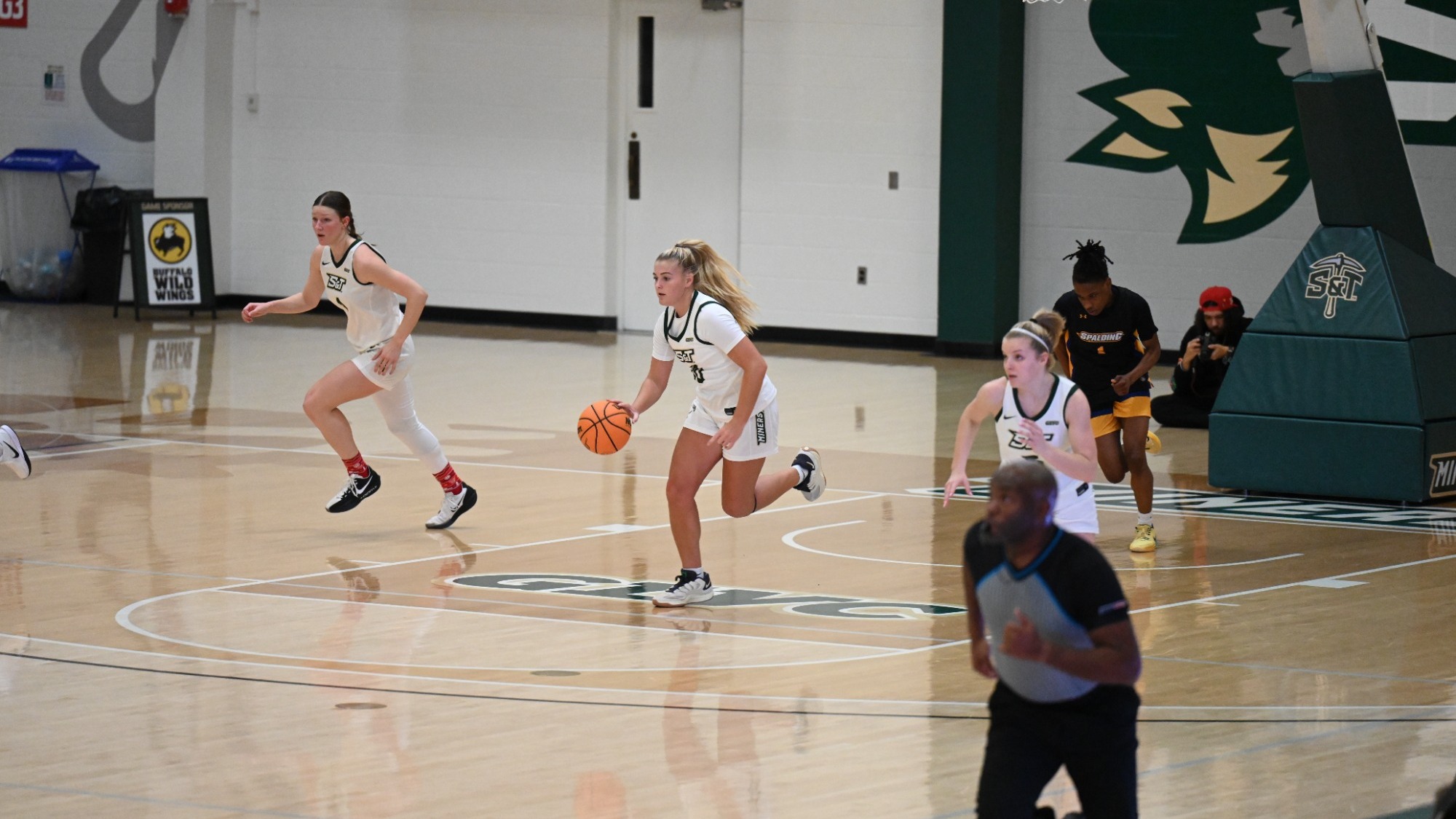 Adrianne Tolen dribbling the ball down the court at Gibson Arena with Norah Gum to the left of her and Ava Casper to the right of her.