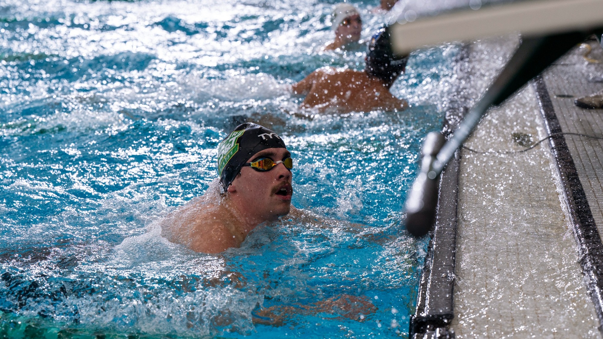 Eli Wetzel of Missouri S&T swimming photographed in the pool after a swim. He is wearing a black swimmers cap and dark goggles