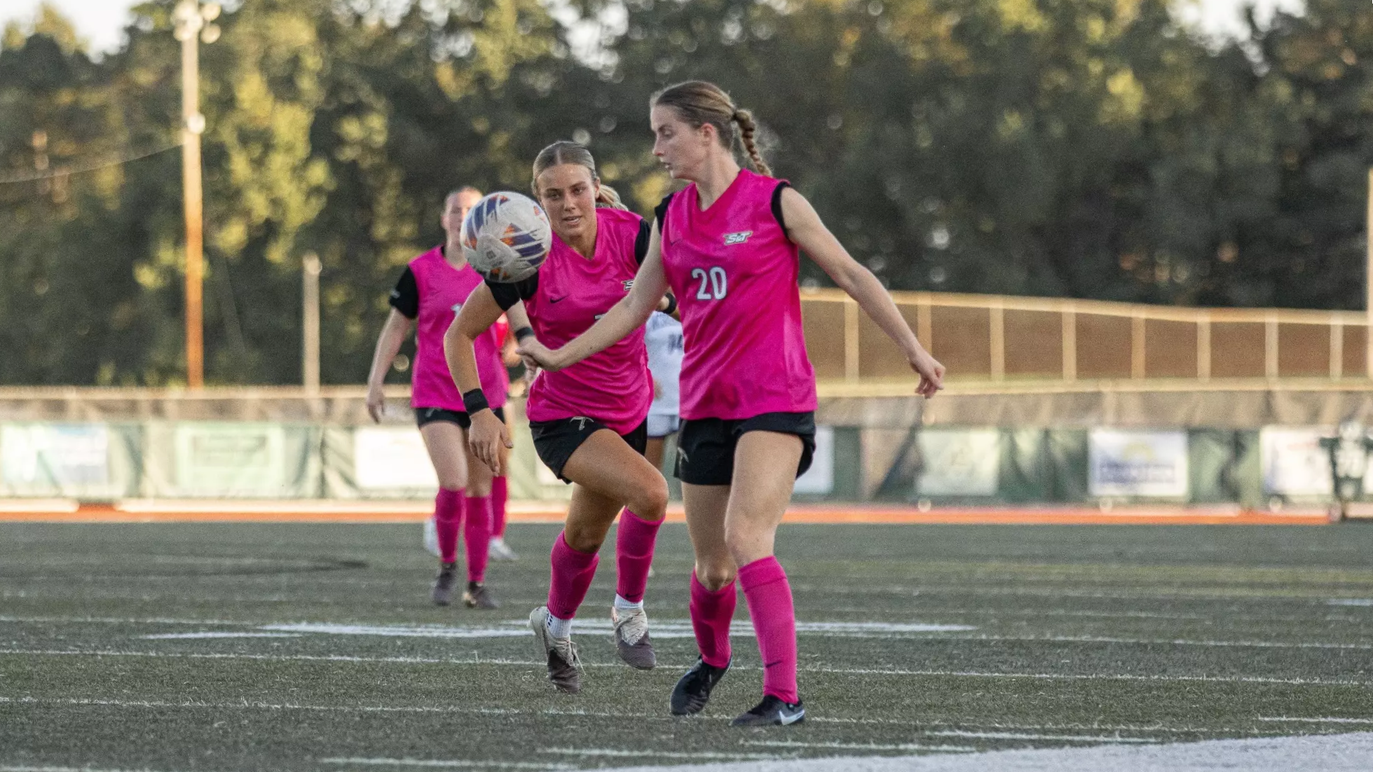 Carlye Bennett in a pink jersey and pink shorts dribbling the soccer ball on a turf field. 