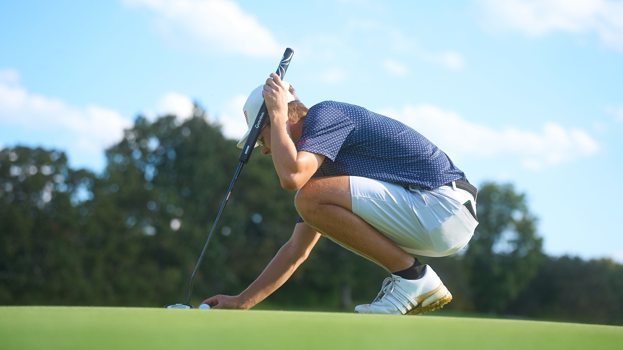 Derek Dulceak of Missouri S&T Athletics photographed squatting on the green and lining up a putt