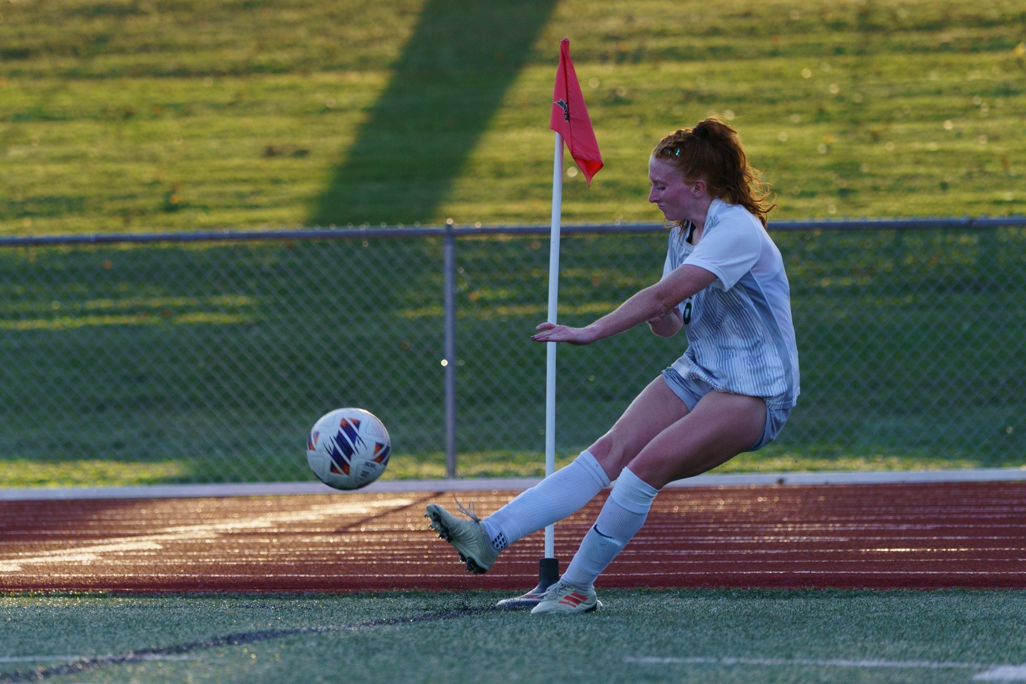 Aubrey Case punting a corner kick with her right foot. She is wearing a white jersey and white shorts