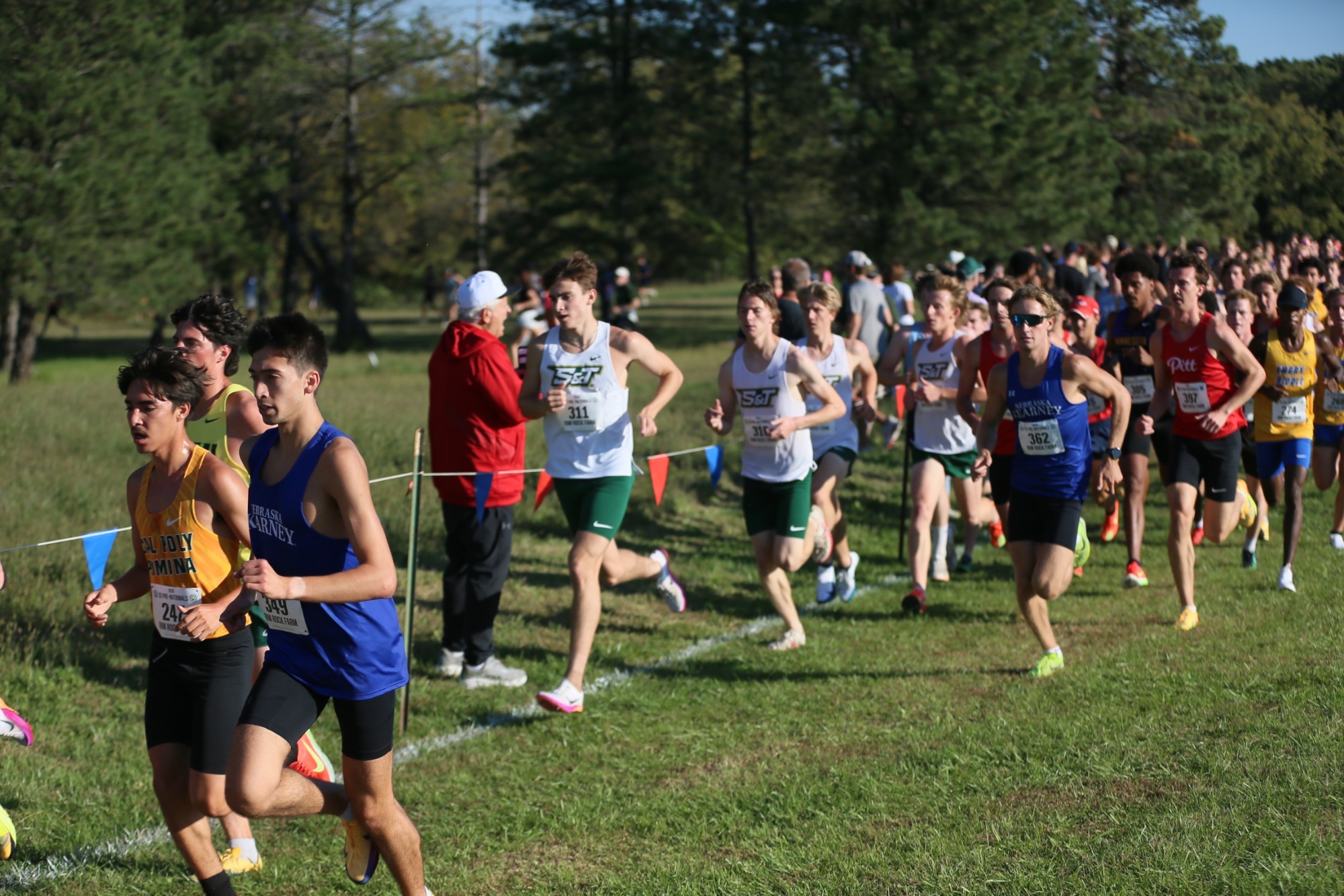 Jack Janovick, Cole Reinties, Robert Falkner and Spencer Pye all running with white jerseys and green shorts. They are running on grass in a group of other runners. 