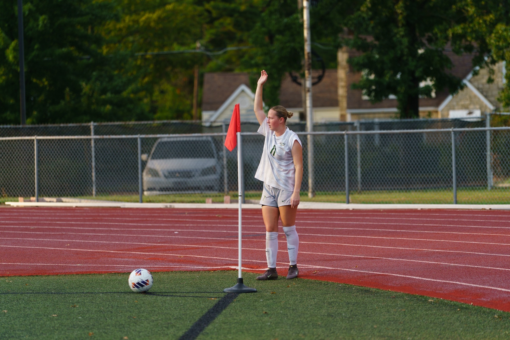 Ella Kramer in a white jersey and white shorts holding her right arm straight up, preparing to chip in a corner kick. 