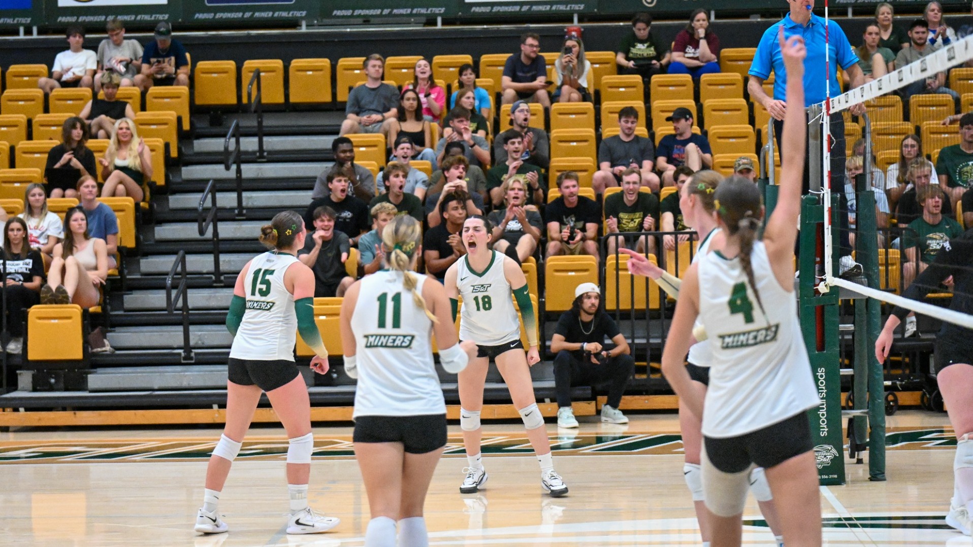 Selin Ozdemir of Missouri S&T Women's volleyball photographed wearing a white uniform and cheering after getting a kill during match in Gibson Arena while her teammates and the home crowd celebrate as well.