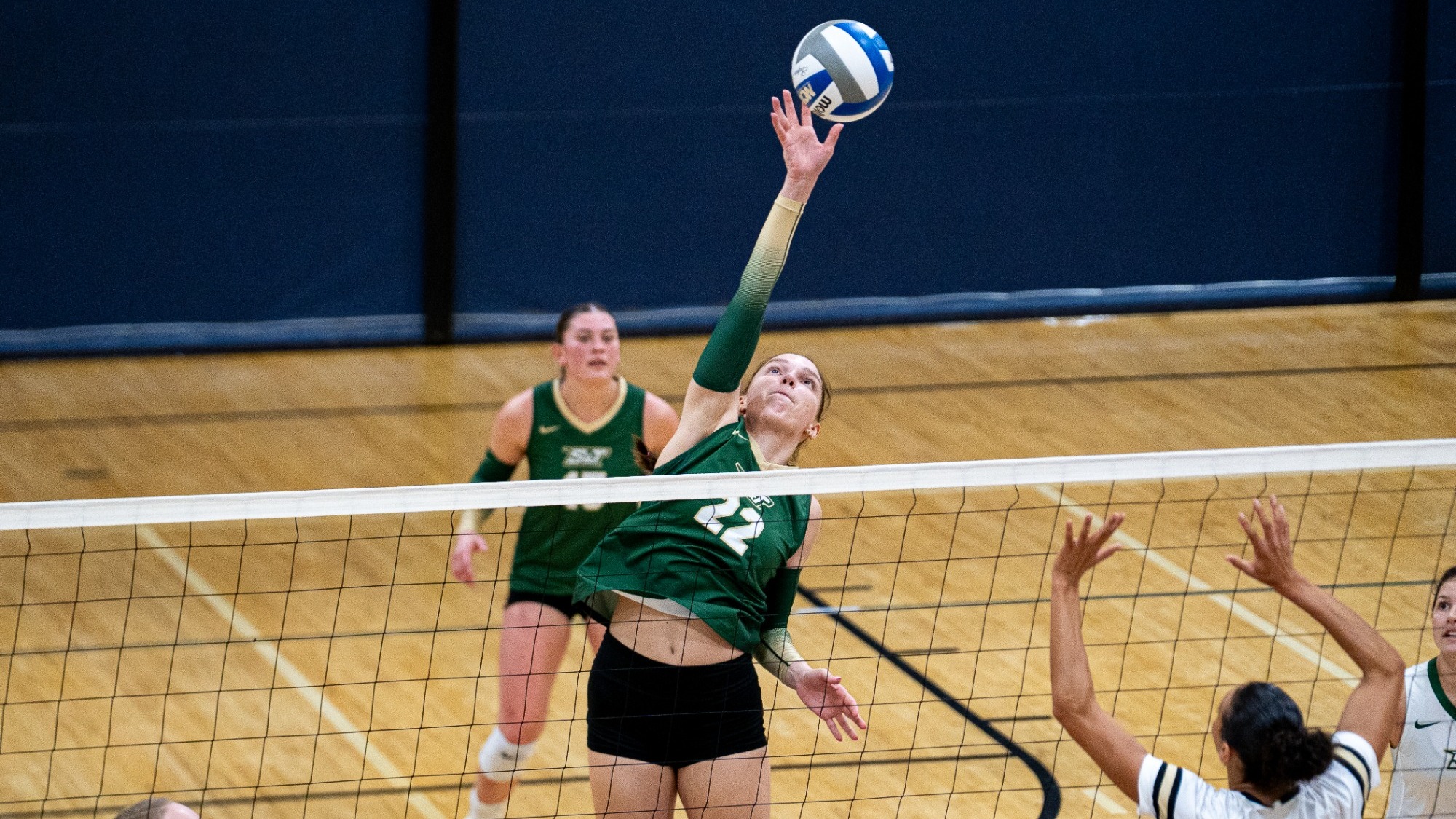 Madison Smith of Missouri S&T Women's Volleyball photographed wearing a green jersey and jumping to attack a volleyball during a match at the Midwest Region Crossover