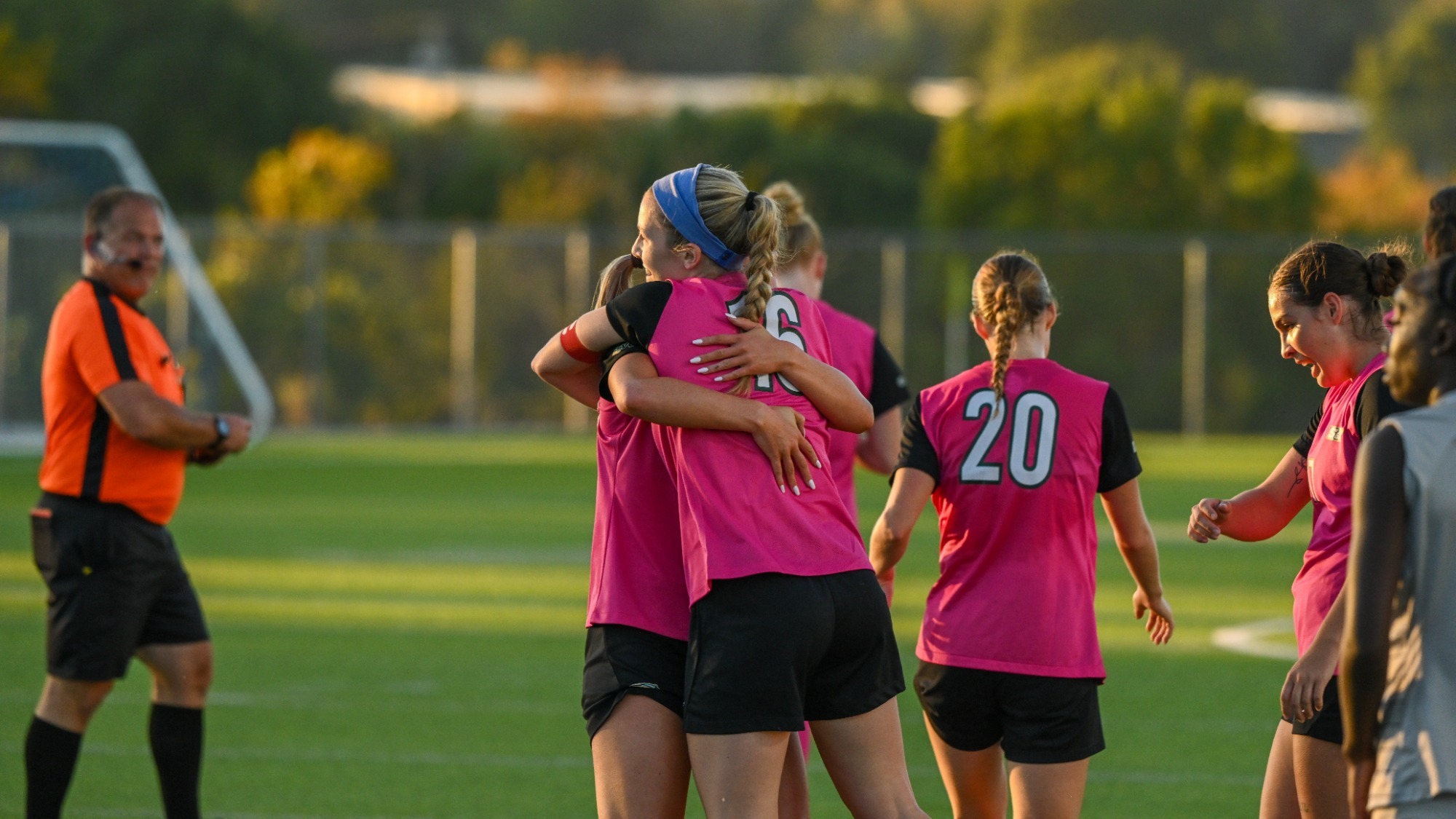 Brooke Bendoff in a pink jersey and pink shorts hugging a team mate after a celebration of a goal. 