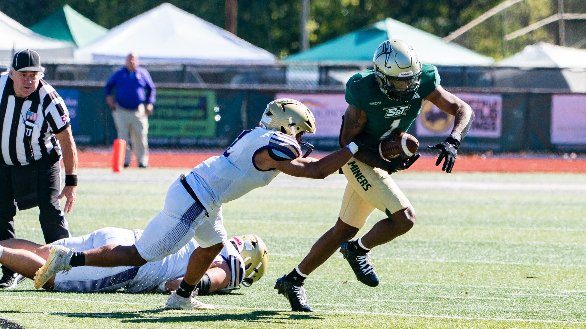 Seneca Bradley of Missouri S&T Football photographed wearing a green uniform and gold helmet. He is running with the ball in hand after recovering a fumble.