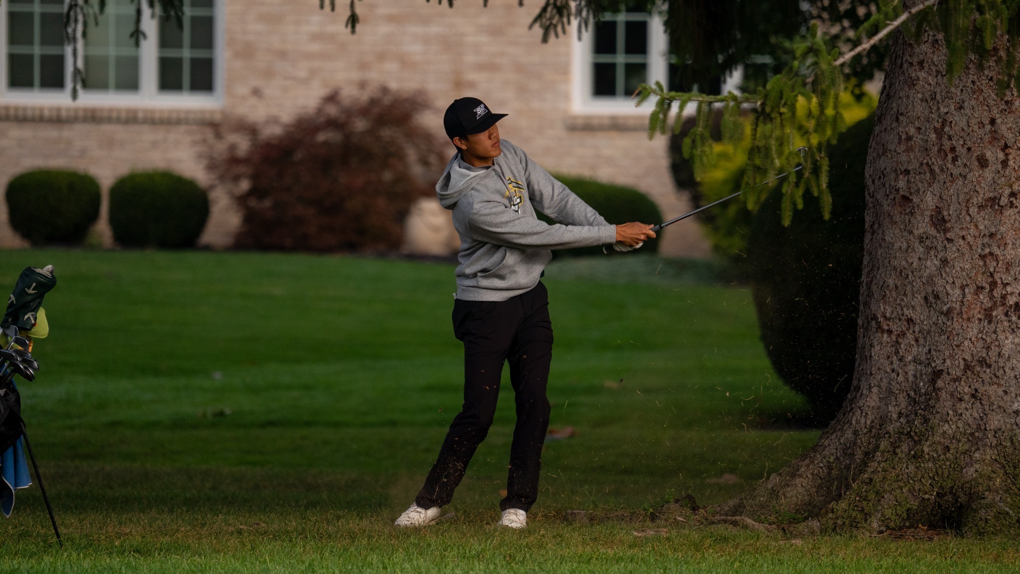 Andy Su of Missouri S&T golf photographed mid-backswing. He is wearing a grey Missouri S&T hoodie and black baseball cap
