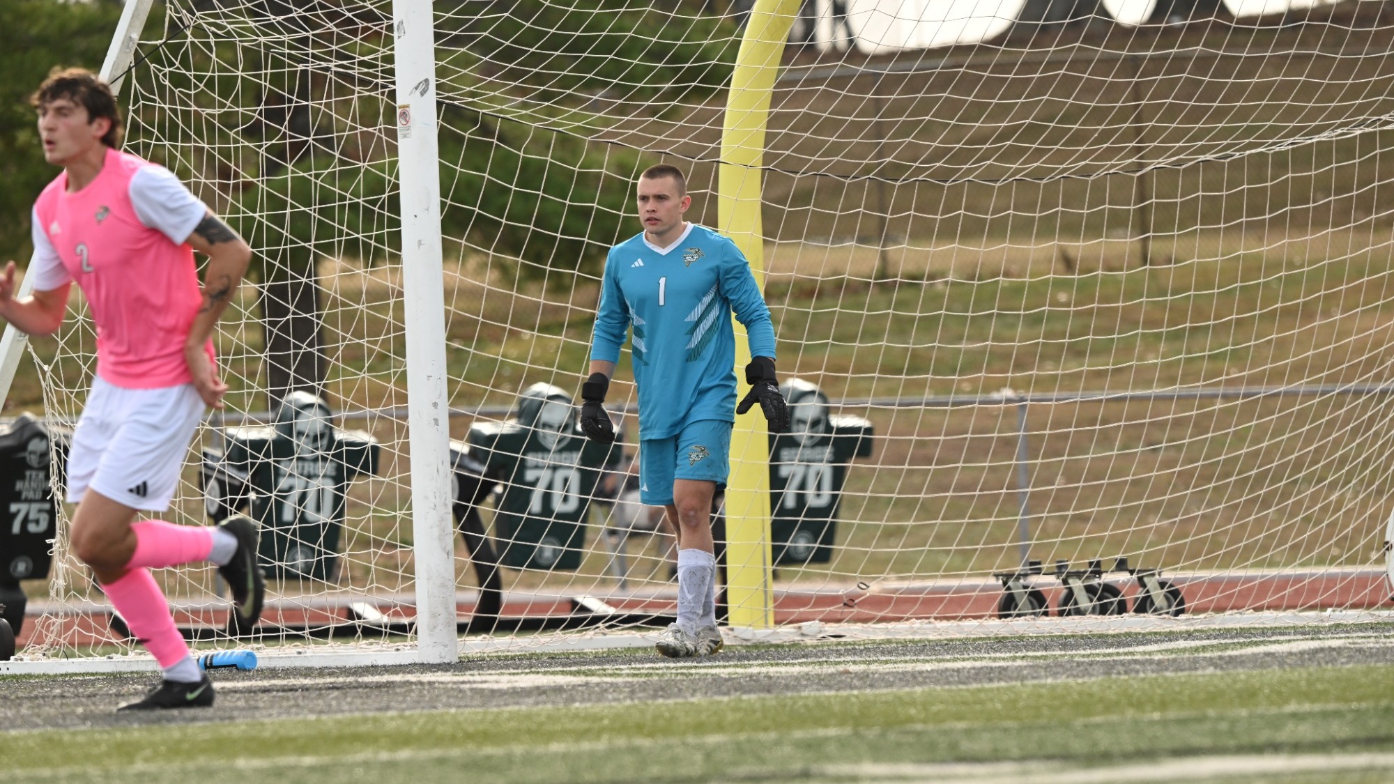 Goalie, Cavitt Bruhn in a blue jersey and blue shorts with white socks and shin guards walking out from the goal exhaling a deep breath.