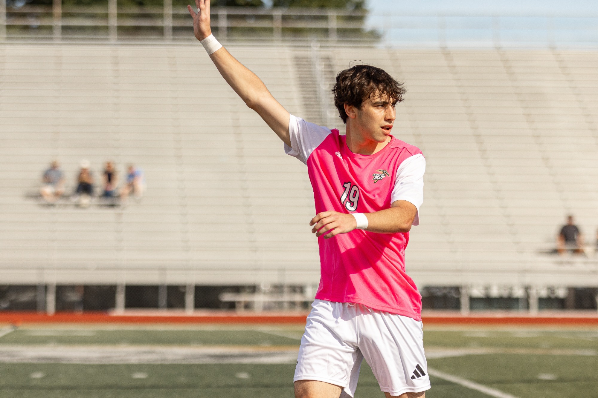 Juliano Costa in a pink jersey raising his hand to get passed the ball 