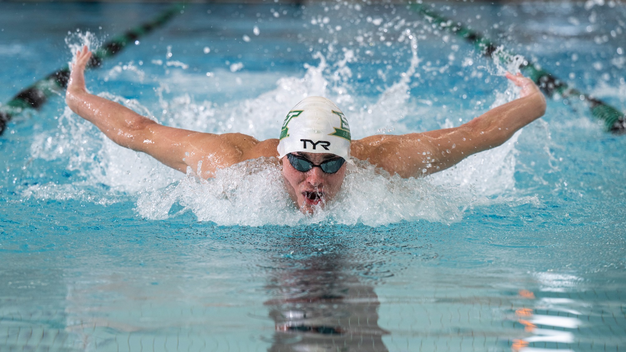 Nic Mahlerbe of Missouri S&T swim photographed wearing a white swim cap and goggles while doing the butterfly stroke in the S&T pool at Gale Bullman