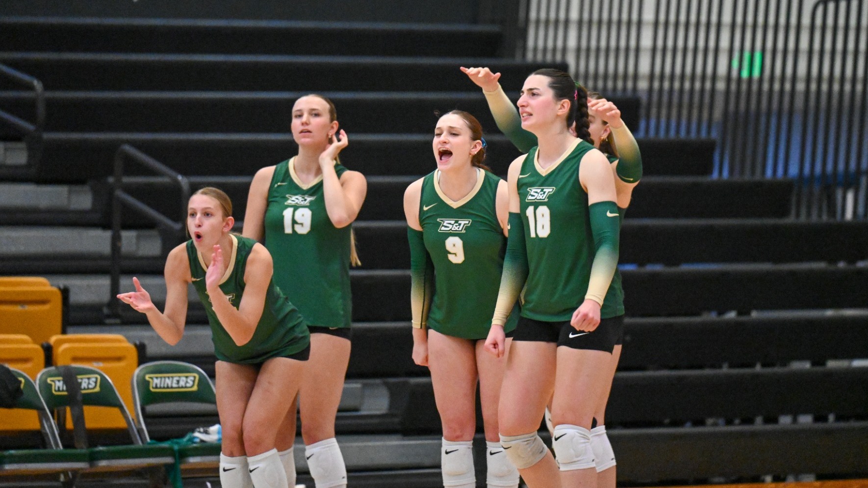 Group Photo of Missouri S&T Women's Volleyball team cheering and clapping while wearing green uniforms
