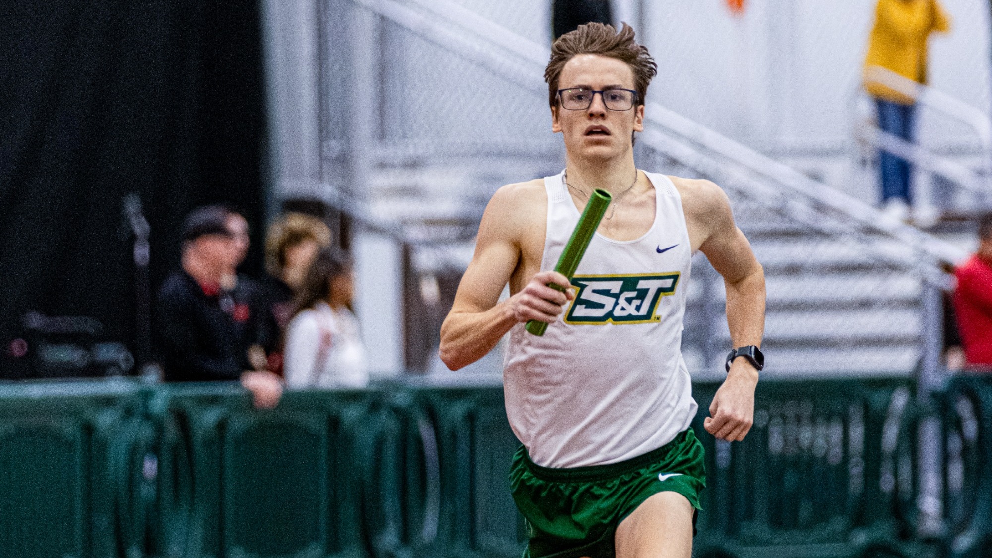 Missouri S&T distance runner Andrew Bacon running the 4000m Distance Medley Relay with a baton in his right hand at the Bearcat Invitational.