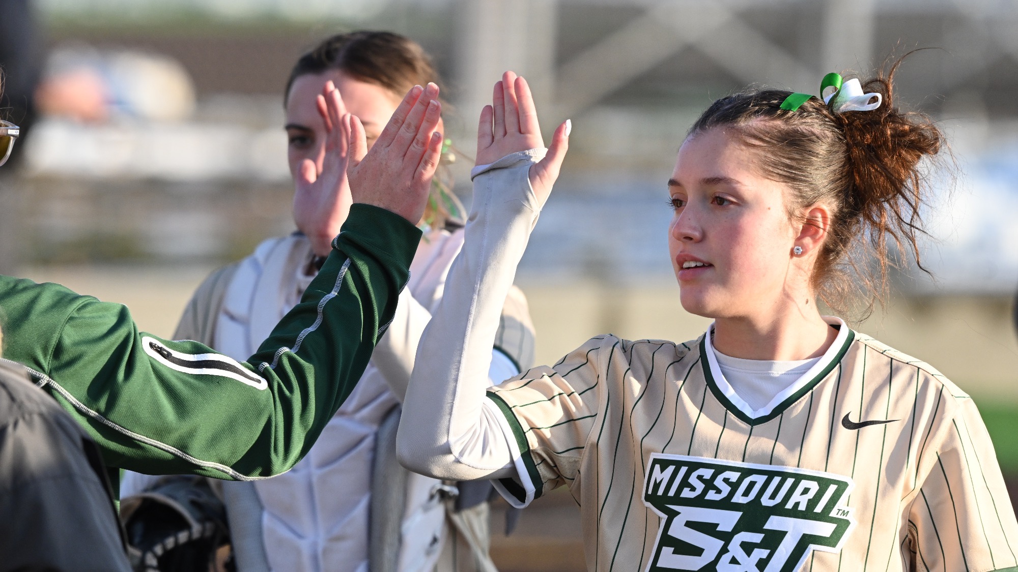 Missouri S&T softball player Joselyn Ulloa in gold stripes jersey giving high five to coach on the field during the Branson Lead Off Classic.