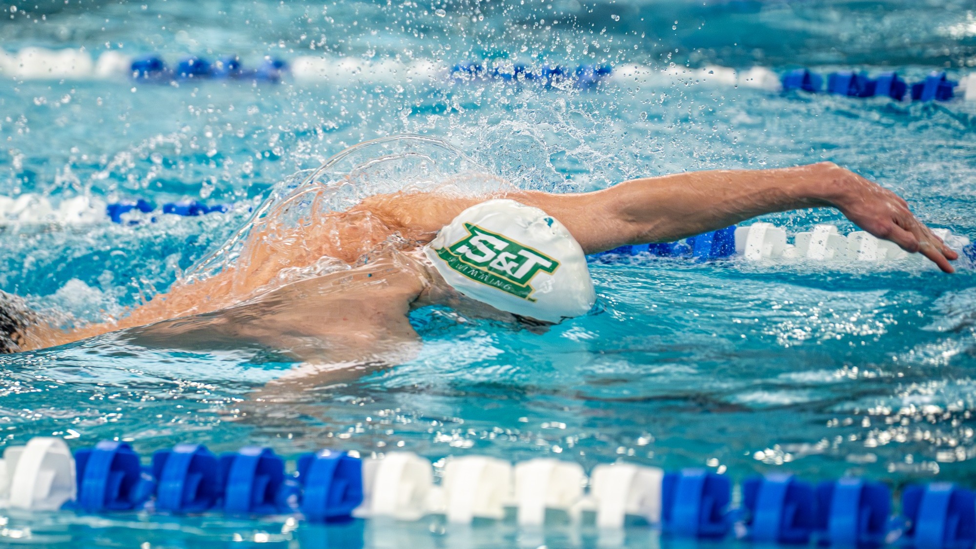 Missouri S&T men's swimmer racing the freestyle with his head down in the water and wearing a white S&T cap during the GLVC Championships