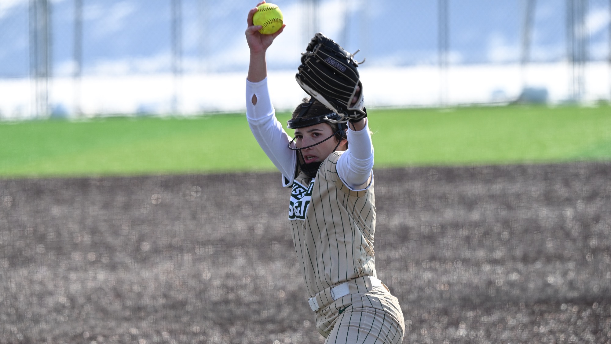 Missouri S&T softball player AJ Agers in the gold jersey mid-pitch at the Branson Lead Off Classic.