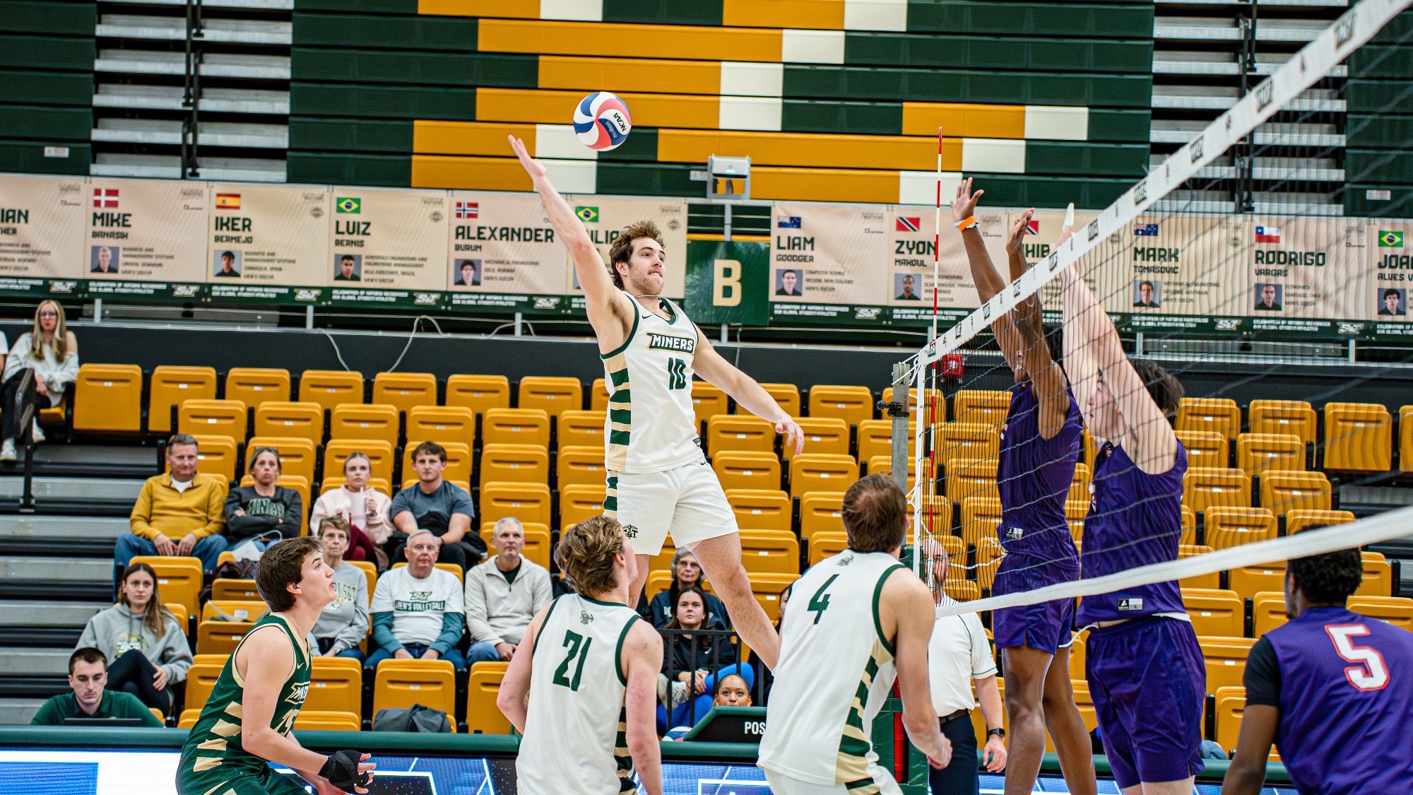 Missouri S&T men’s volleyball athlete Nate Meyer jumping and swinging his right arm at the Volleyball to attack while the Edward Waters opponents jump at the net in attempt to block