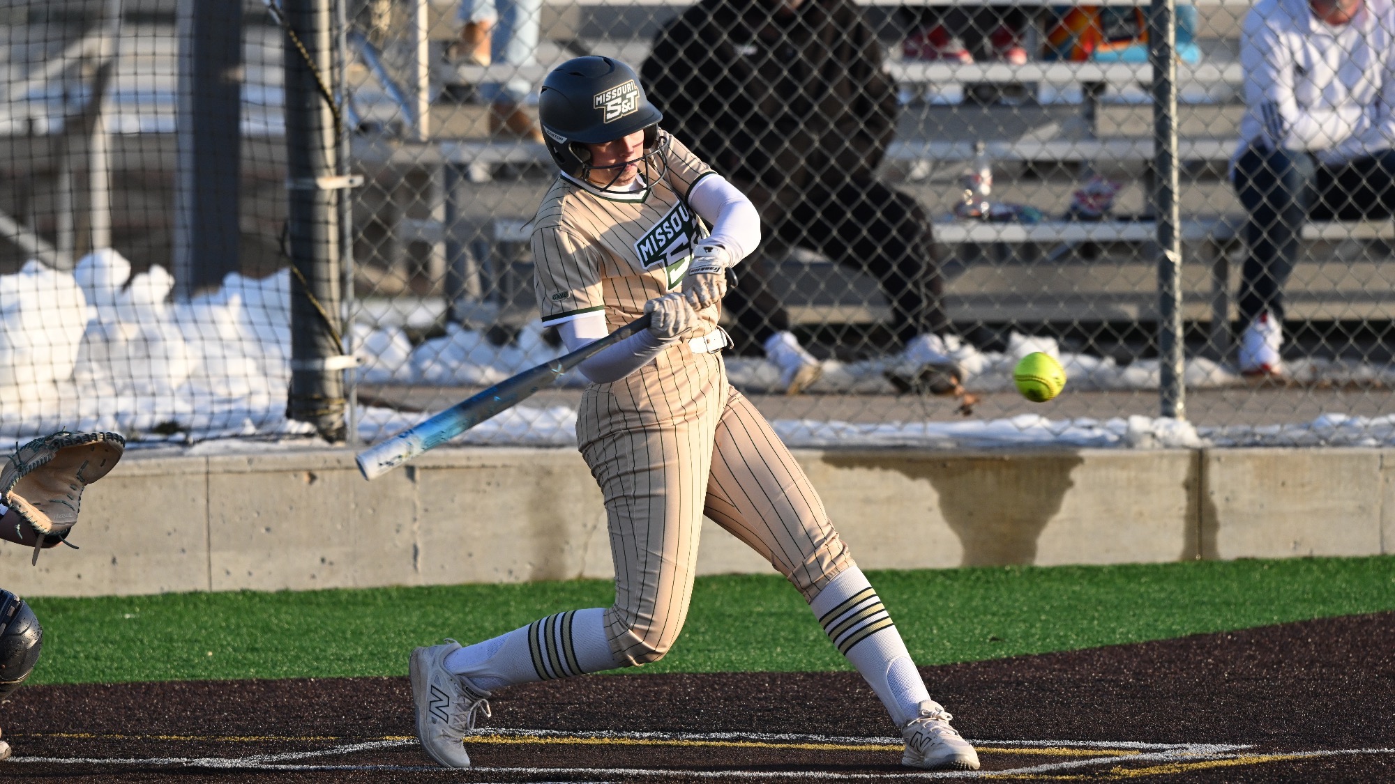 Missouri S&T softball player Taylor Nelson up to bat in gold S&T pinstripes jersey hitting the softball during a game.