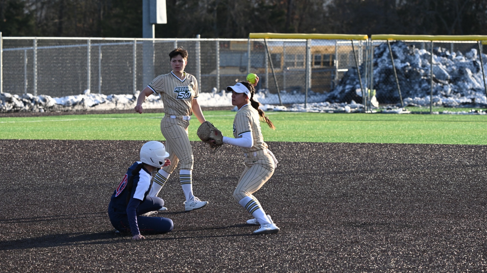 Missouri S&T second baseman Claire Lopez prepares to throw the ball while wearing a gold Miners jersey as an opposing runner in a navy blue jersey slides into second base.