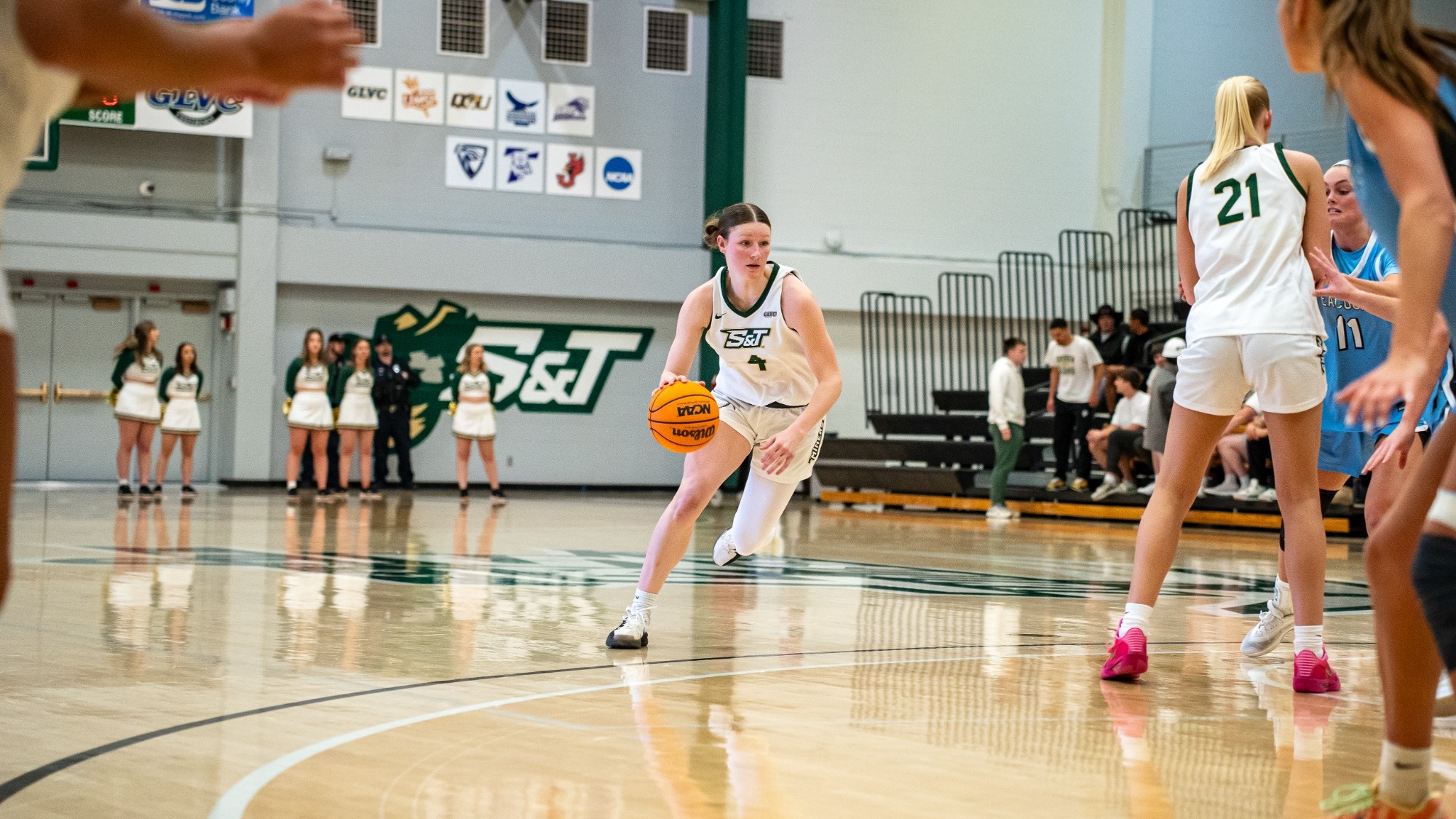 Missouri S&T women's basketball player Norah Gum in the white jersey on the perimeter driving to the hoop.