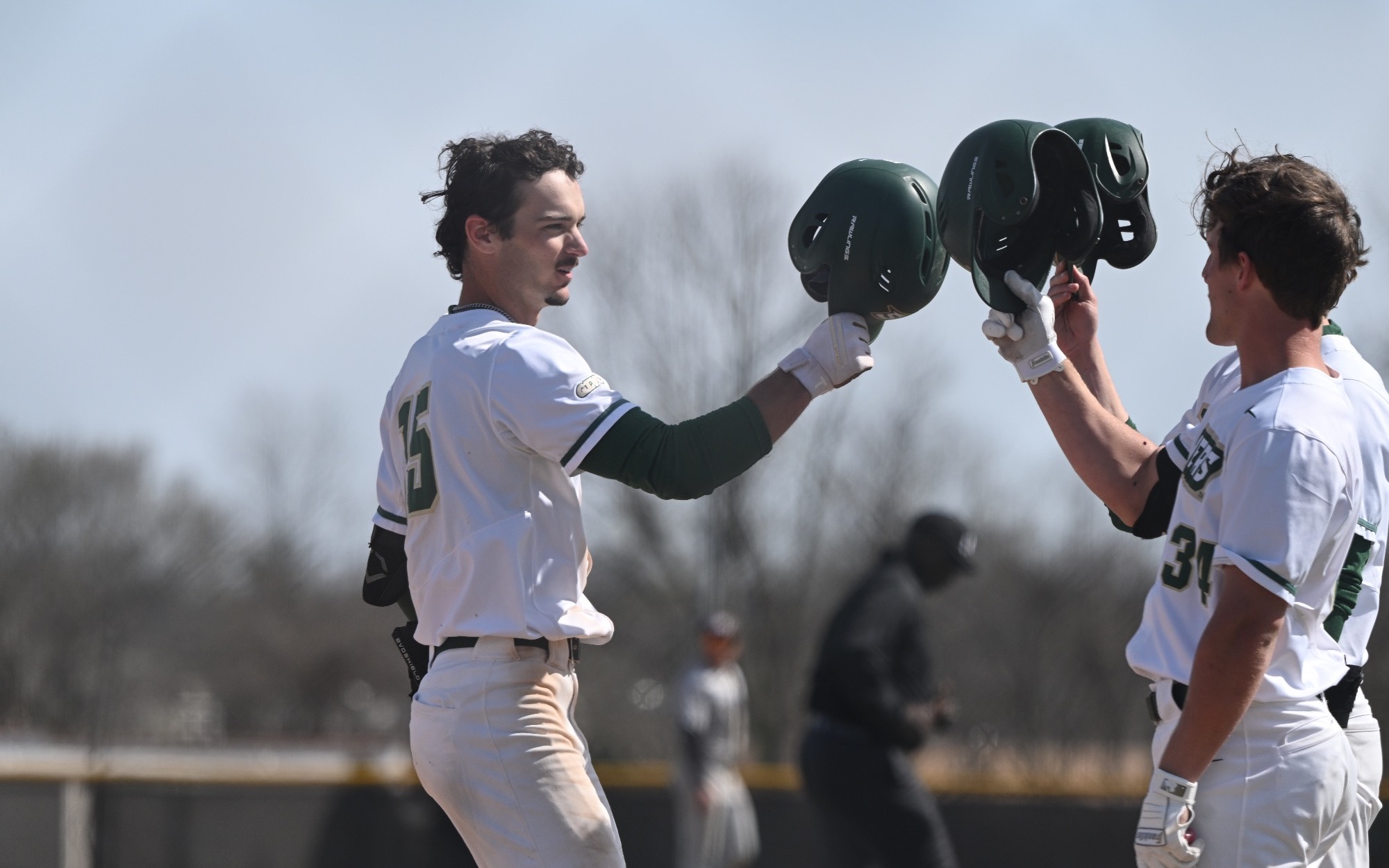Missouri S&T baseball player Garrett Meyer is photographed with his batting helmet in his hand, extending it out to two of his teammates to touch helmets as a celebration after he hit a choke run