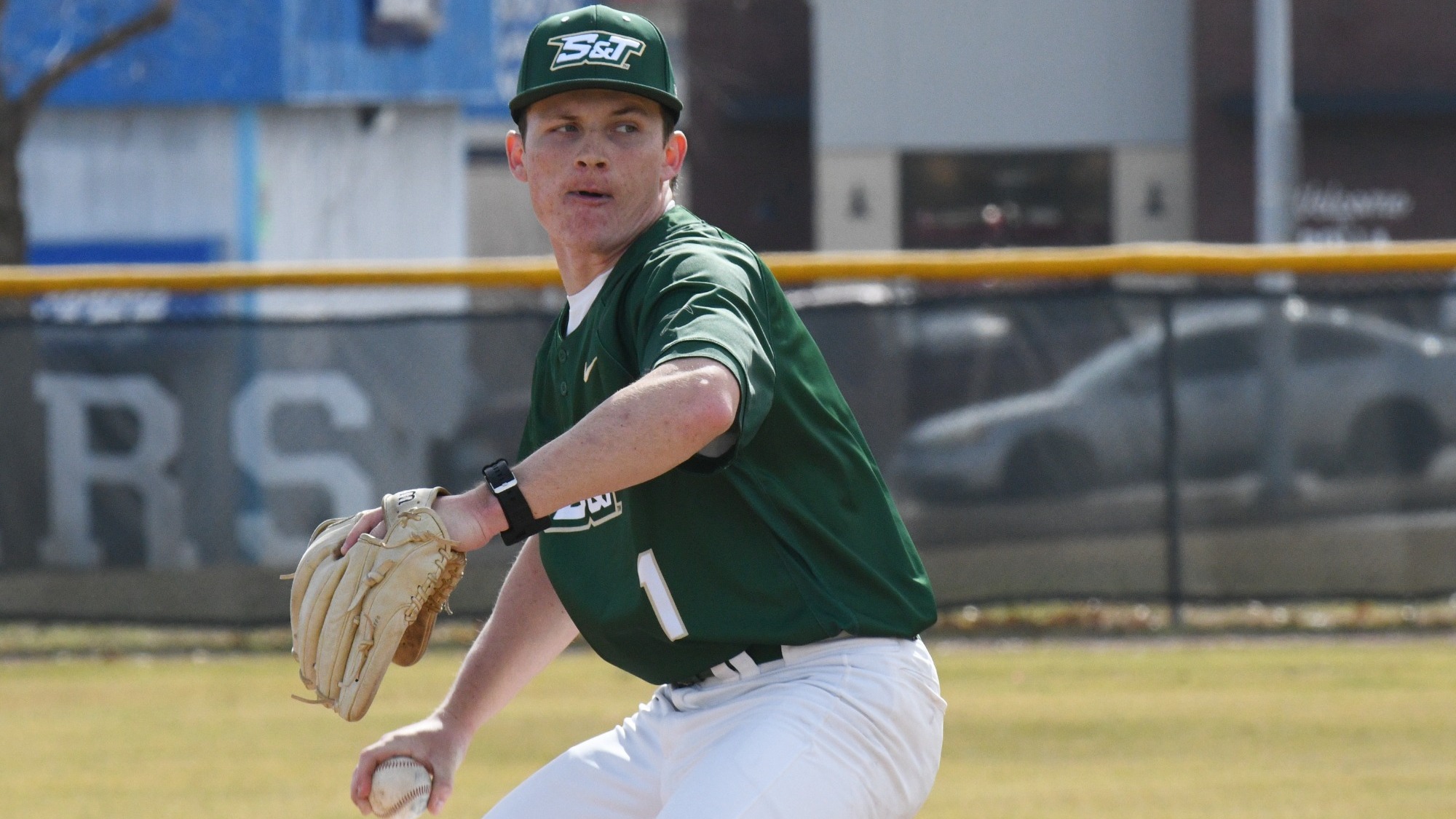 Missouri S&T Baseball player Andrew Hedgecorth winds up to get ready to throw a pitch during a baseball game in the ballpark at S&T. He wears a green uniform with a white number one on it and a green baseball cap with the S&T logo on it