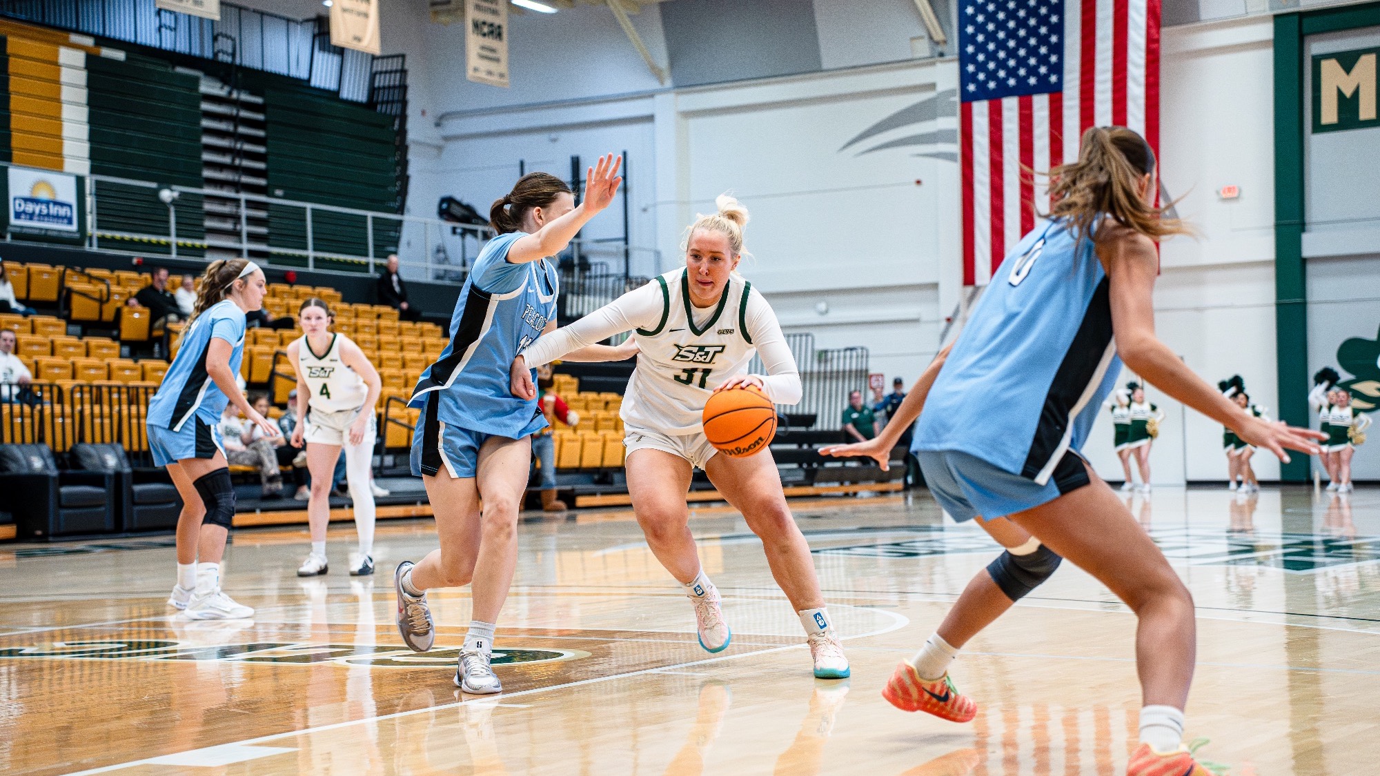 Missouri S&T sophomore forward Anna Gilbertson, wearing a white Miners jersey, drives toward the basket while dribbling through two Upper Iowa defenders in baby blue uniforms during a game inside Gibson Arena.