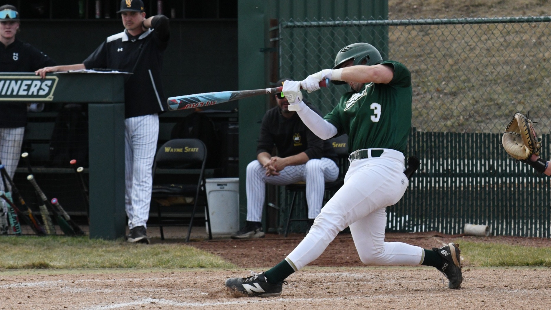 Missouri S&T baseball player Keaton Scott is photographer mid-swing during an at bat at the ballpark at S&T. He is on his follow through with the bat extended out in front of him and the baseball shown in the air above him. He is wearing a green Missouri S&T baseball uniform and matching green hat