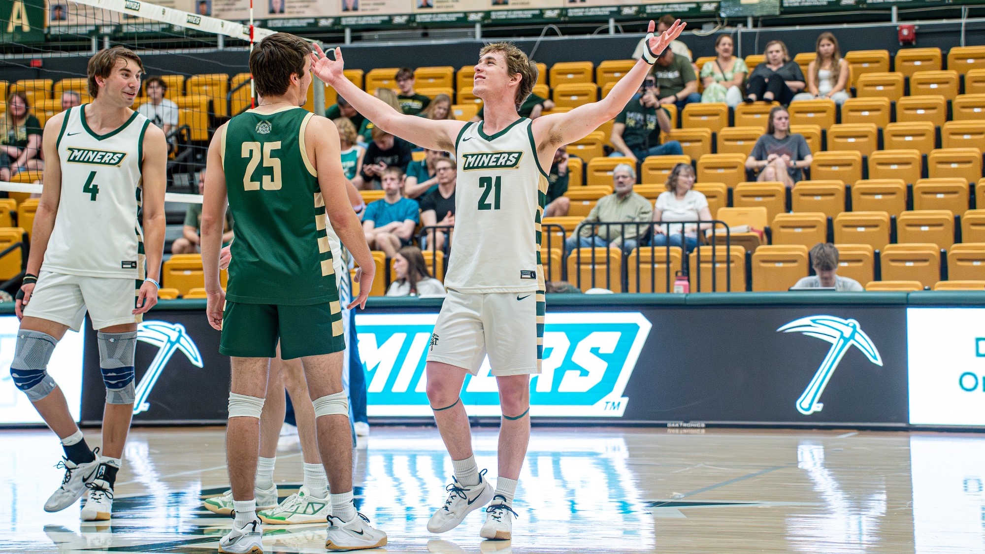 Missouri S&T setter Grant Edmonds, wearing a white Miners jersey, raises his arms in celebration after a point while teammates gather around him on the court in Gibson Arena.