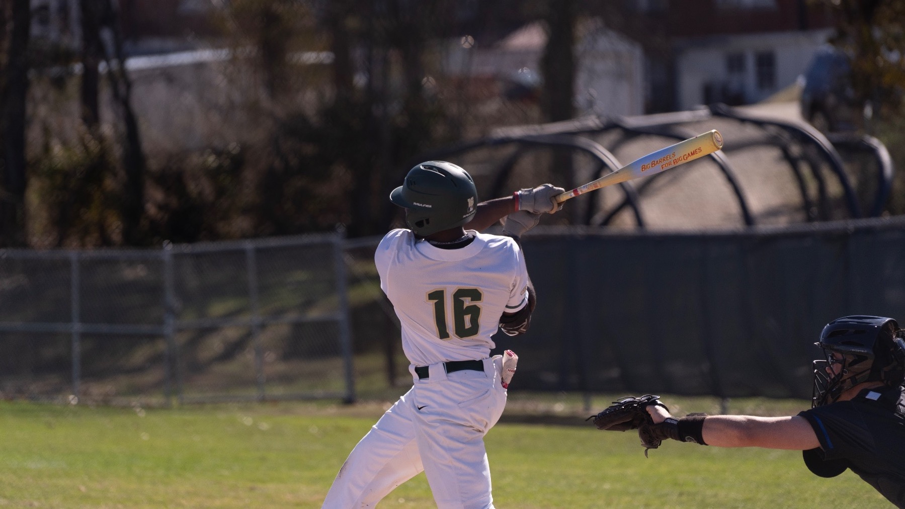 Bricen Smith of the Missouri S&T baseball team is photographed finishing his swing at the plate, with his bat extended high over his shoulder while the catcher reaches forward to receive the pitch behind him.