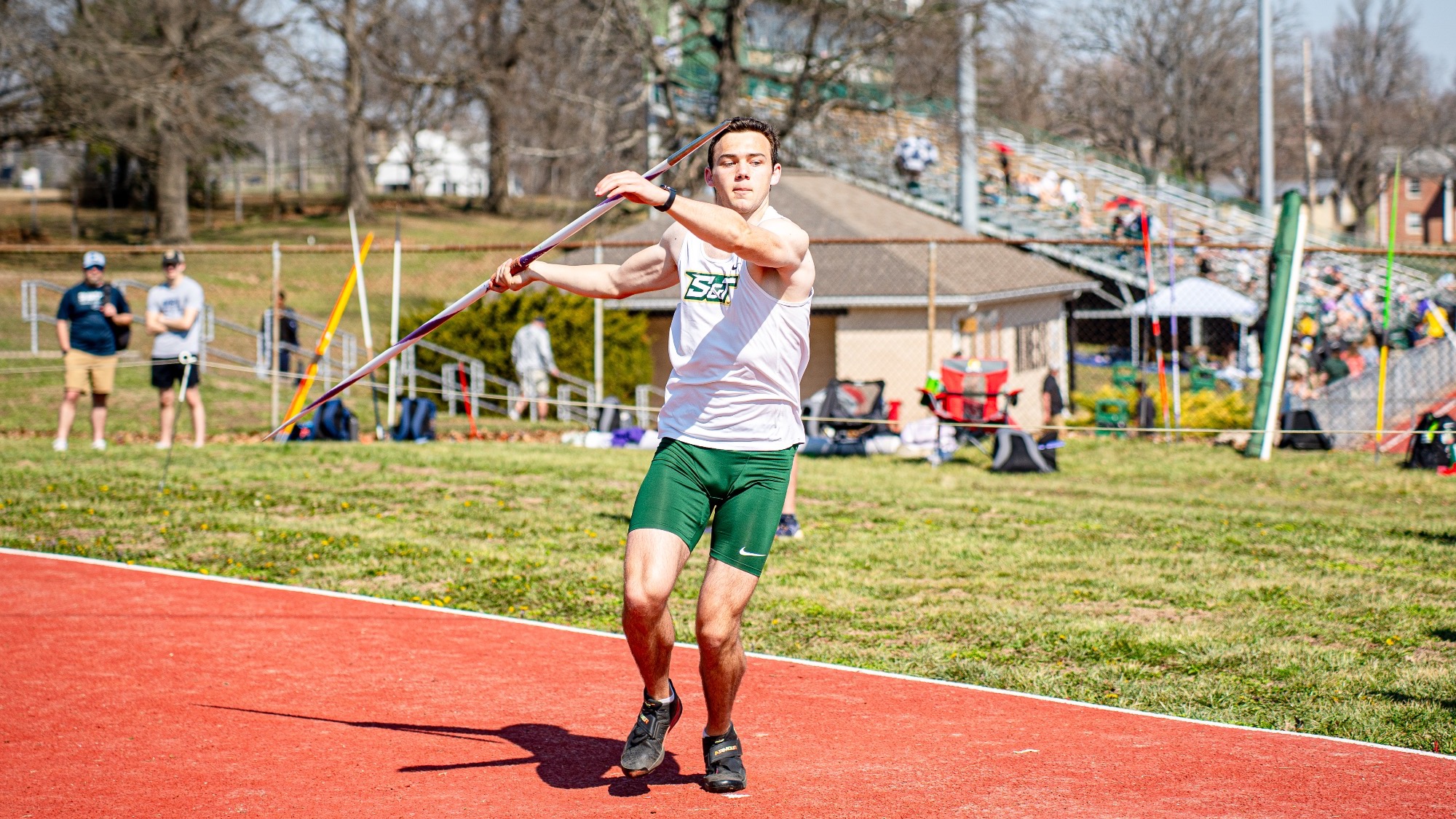 Missouri S&T’s Landon Oelschlaeger prepares to release the javelin during competition at the Miner Invitational, with spectators visible in the background.
