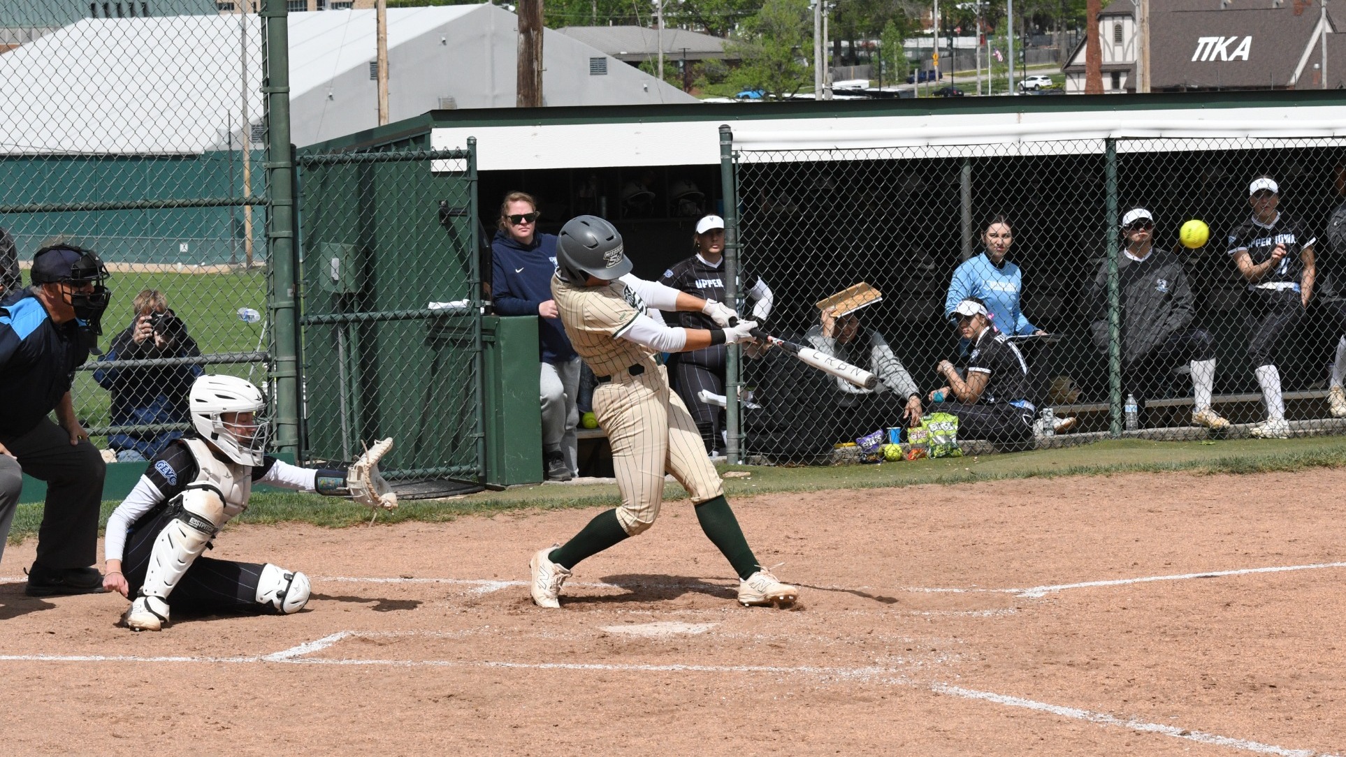 Taylor Nelson, dressed in a gold pin stripe uniform, hits the School Record Home Run during an at bat